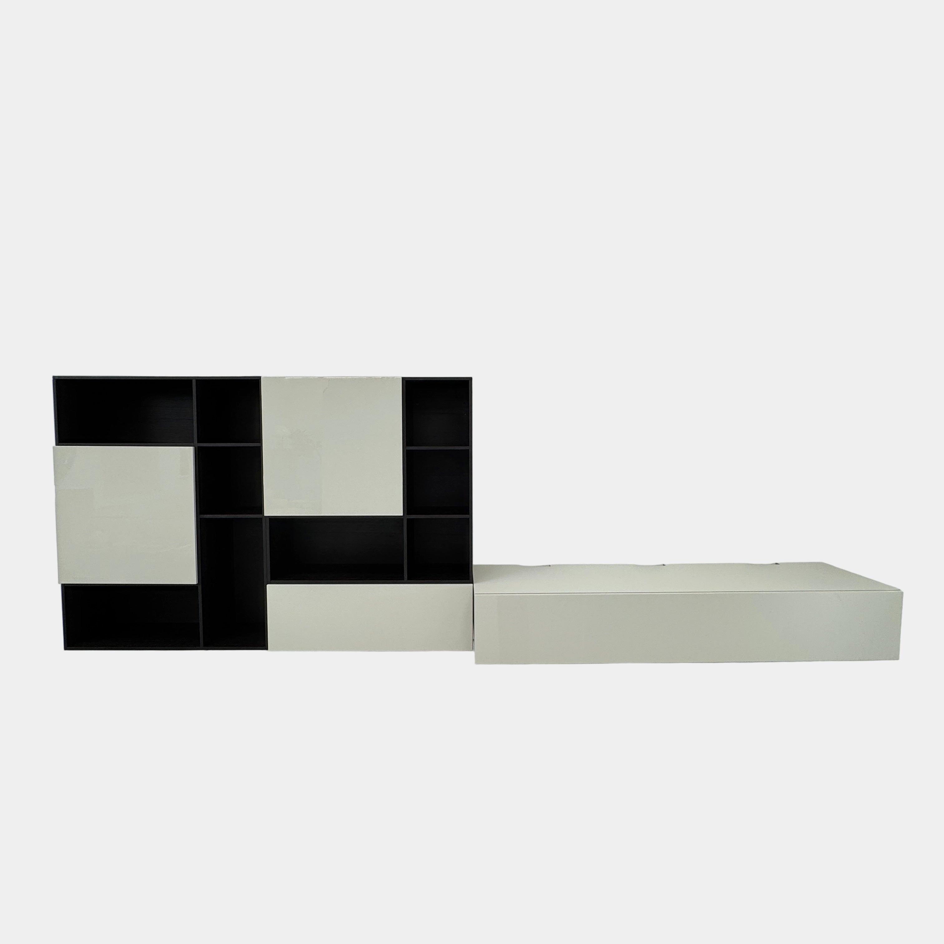 The Lema Selecta Wall Hanging Unit by Lema features black and white open and closed compartments, paired with a low rectangular white storage bench on the right.