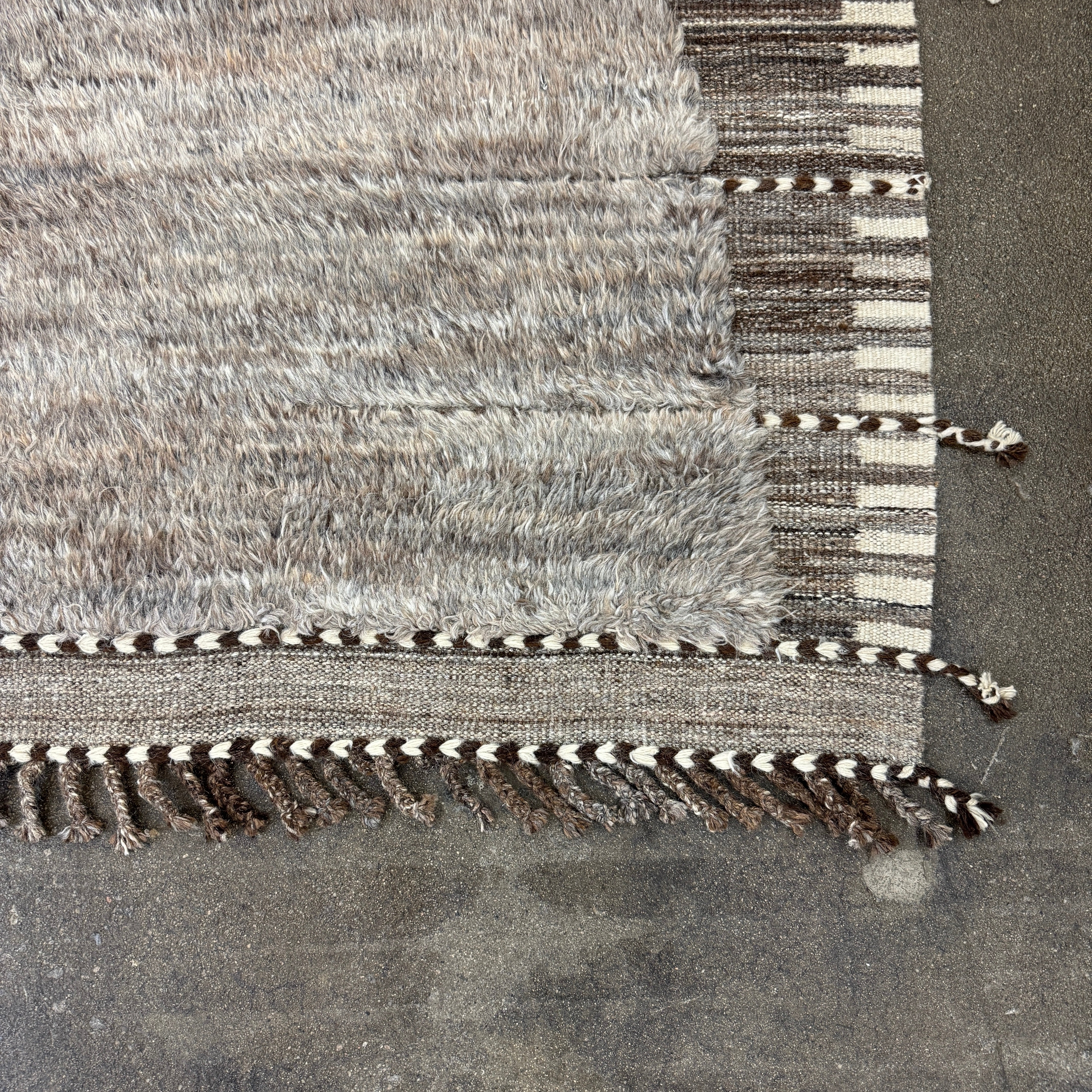 The Mehraban Gilavar Rug (13' x 15'.5") by Mehraban features handwoven, textured neutral tones, fringe tassels on the edges, and striped and patterned designs.