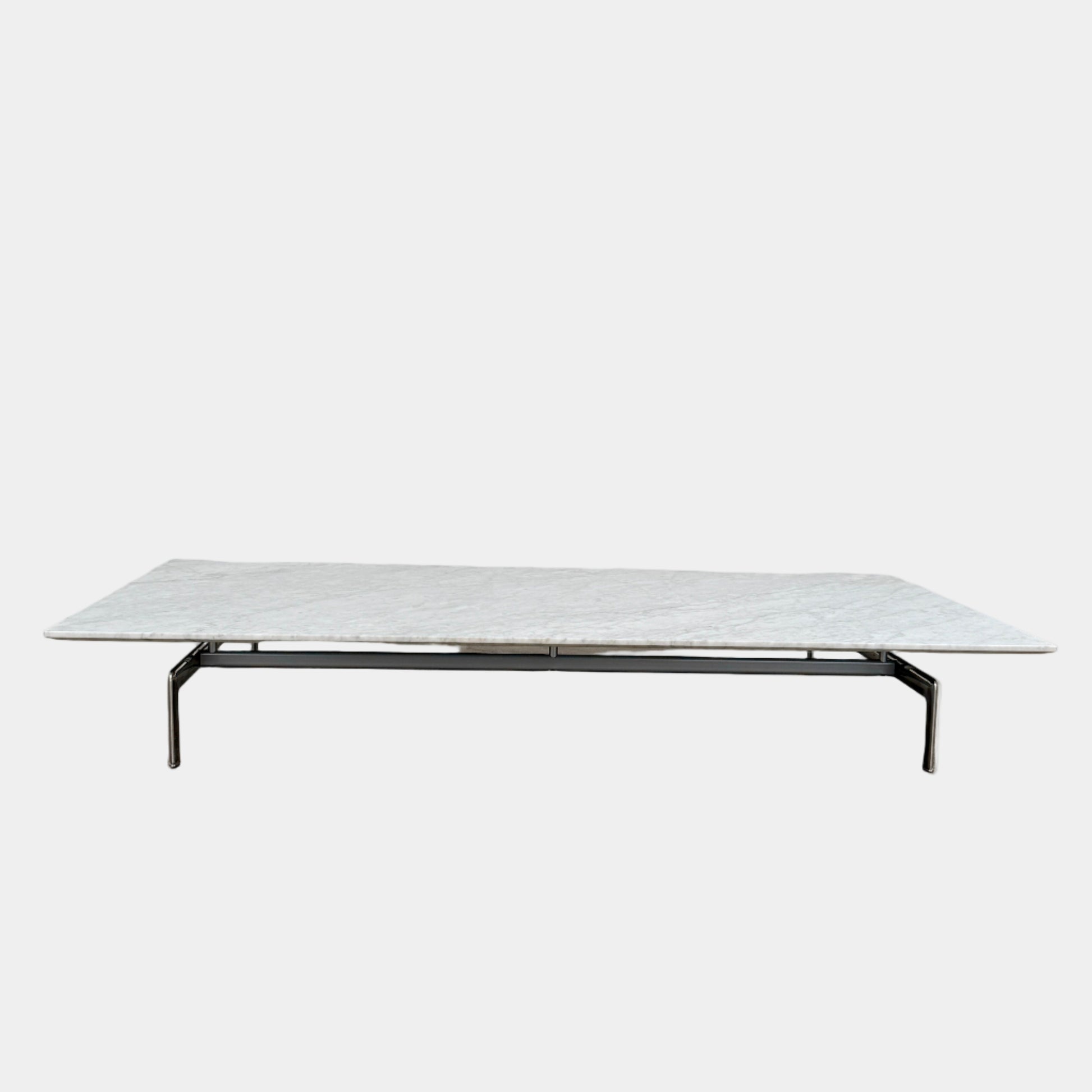 The B&B Italia Diesis Marble Coffee Table by B&B Italia, featuring a low rectangular white marble top and slim metal legs, is placed on a polished concrete floor against a plain white wall.