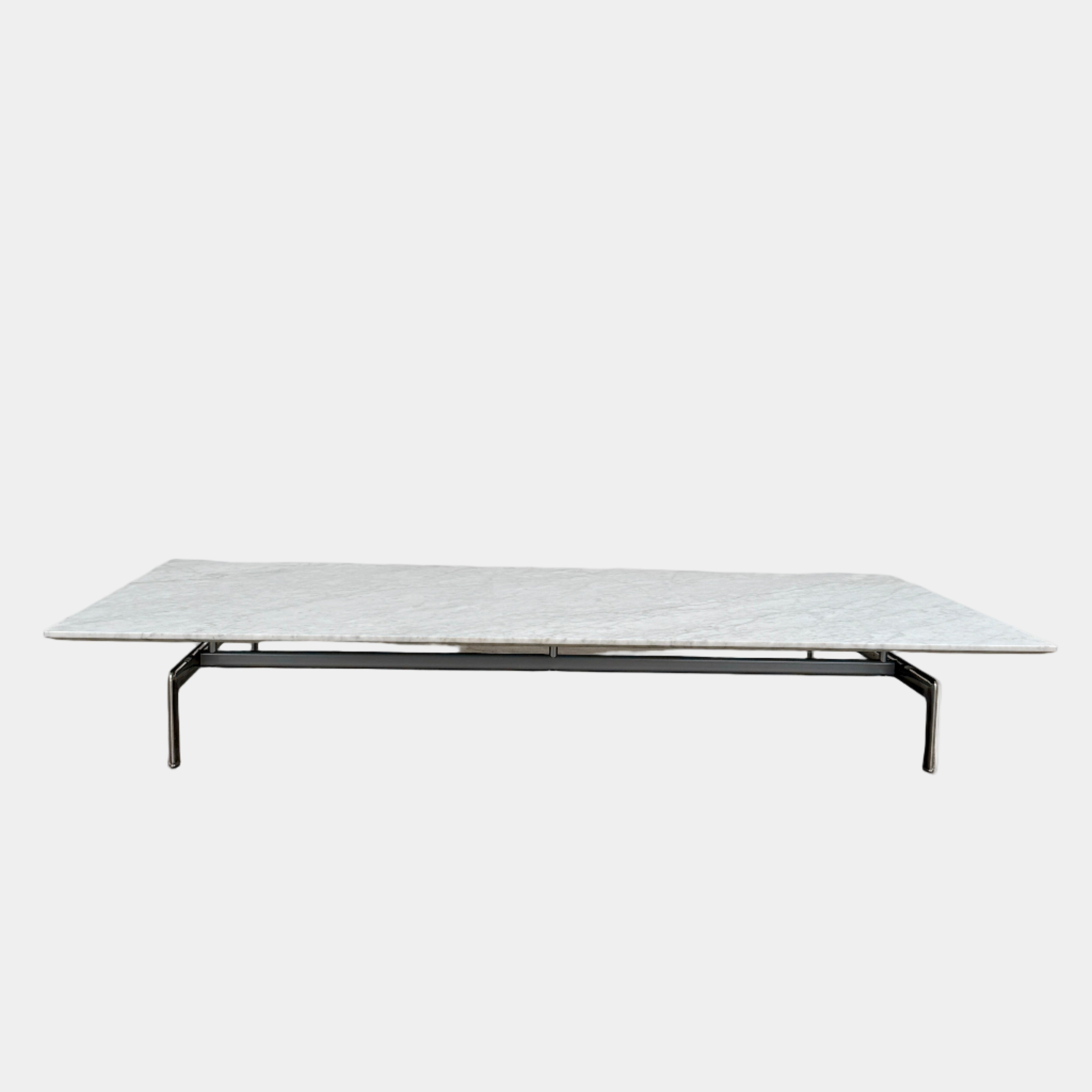 The B&B Italia Diesis Marble Coffee Table by B&B Italia, featuring a low rectangular white marble top and slim metal legs, is placed on a polished concrete floor against a plain white wall.