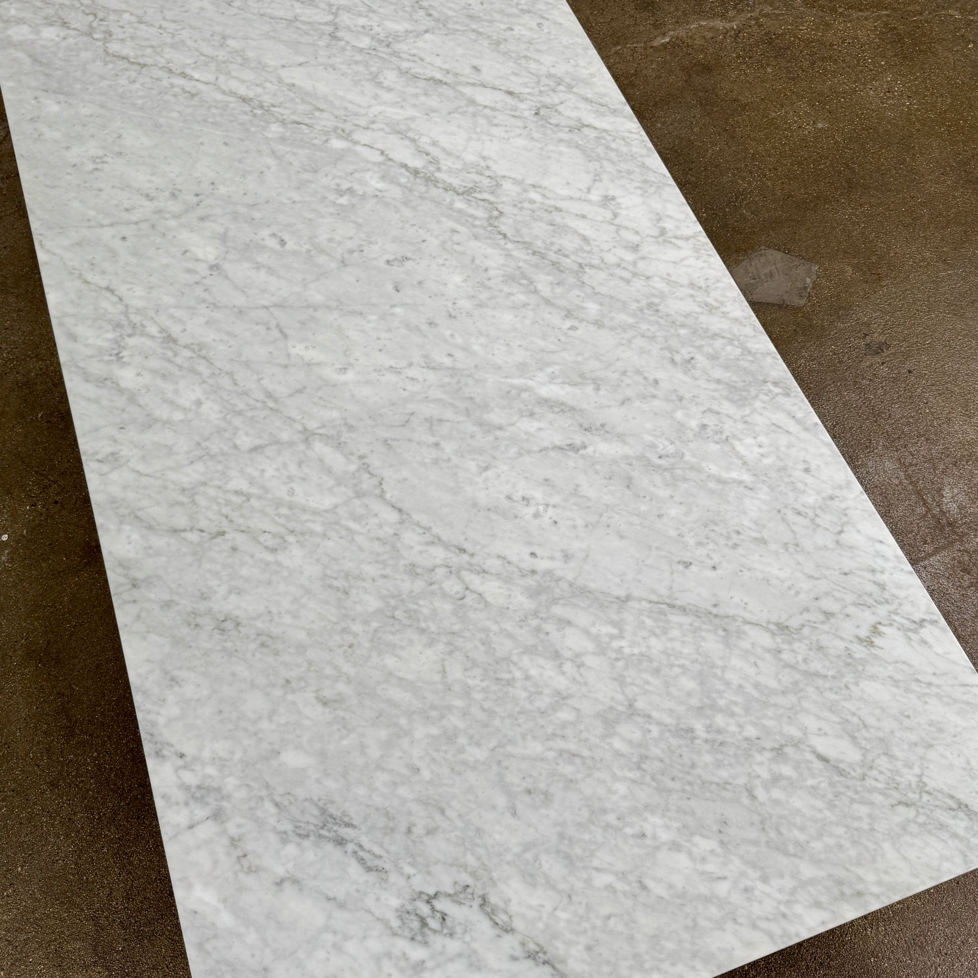 The B&B Italia Diesis Marble Coffee Table by B&B Italia, featuring a low rectangular white marble top and slim metal legs, is placed on a polished concrete floor against a plain white wall.