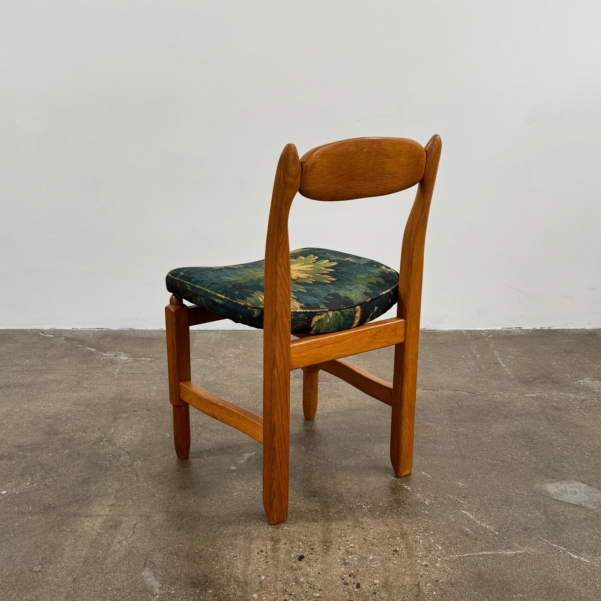 A set of 6 Vintage Votre Maison Guillerme Et Chambron dining chairs in French oak with curved backs and green floral upholstery are shown in two rows of three, highlighting postwar modernist elegance against a white background.
