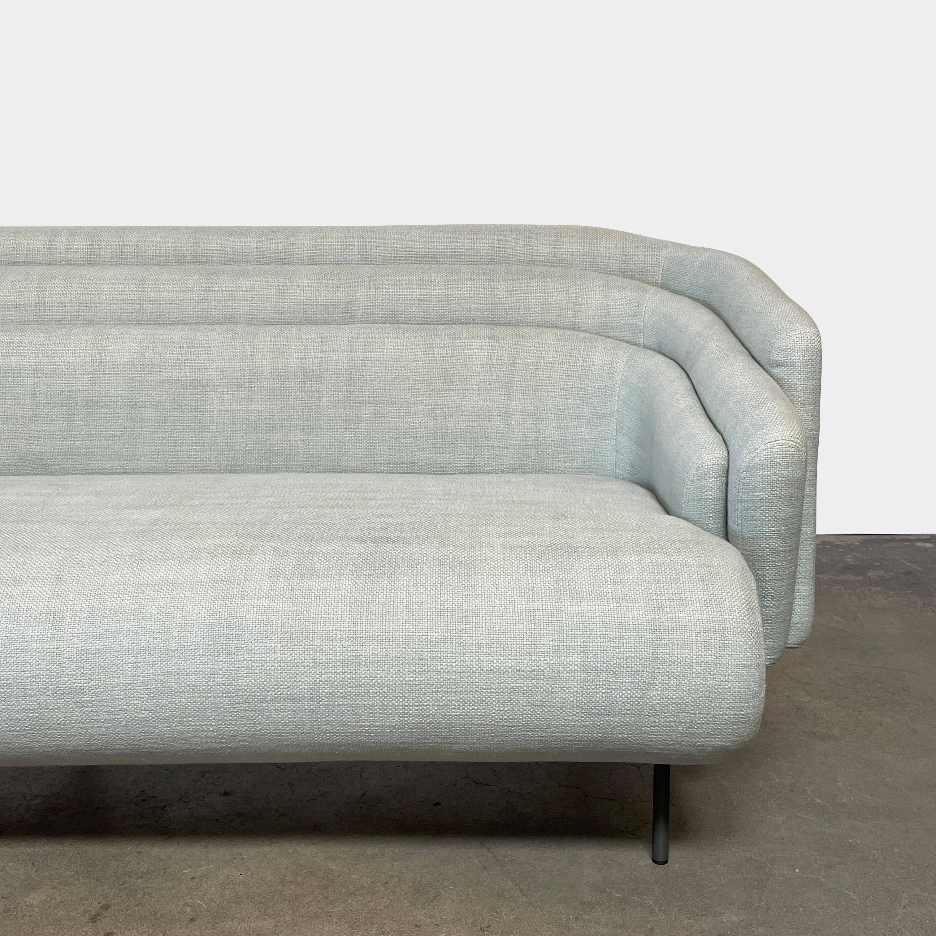 The Delcourt Collection Hug Sofa from the Delcourt Collection offers customizable fabric choices, including a light blue option, and is supported by sleek black legs.
