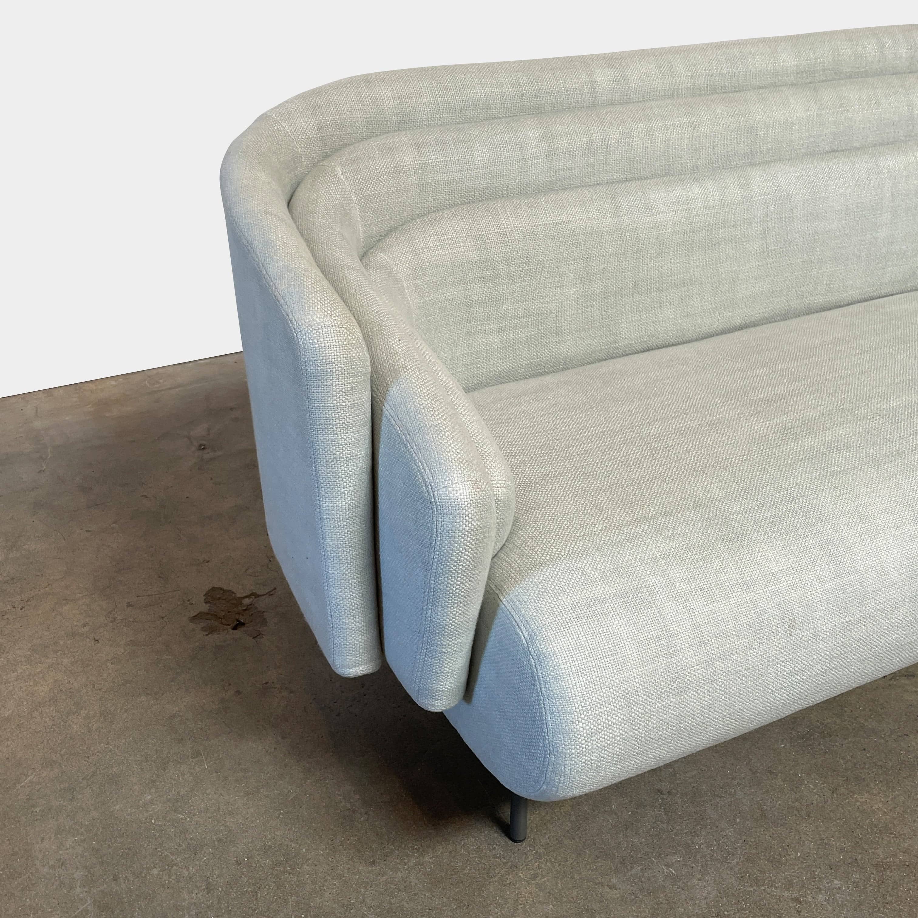 The Delcourt Collection Hug Sofa from the Delcourt Collection offers customizable fabric choices, including a light blue option, and is supported by sleek black legs.
