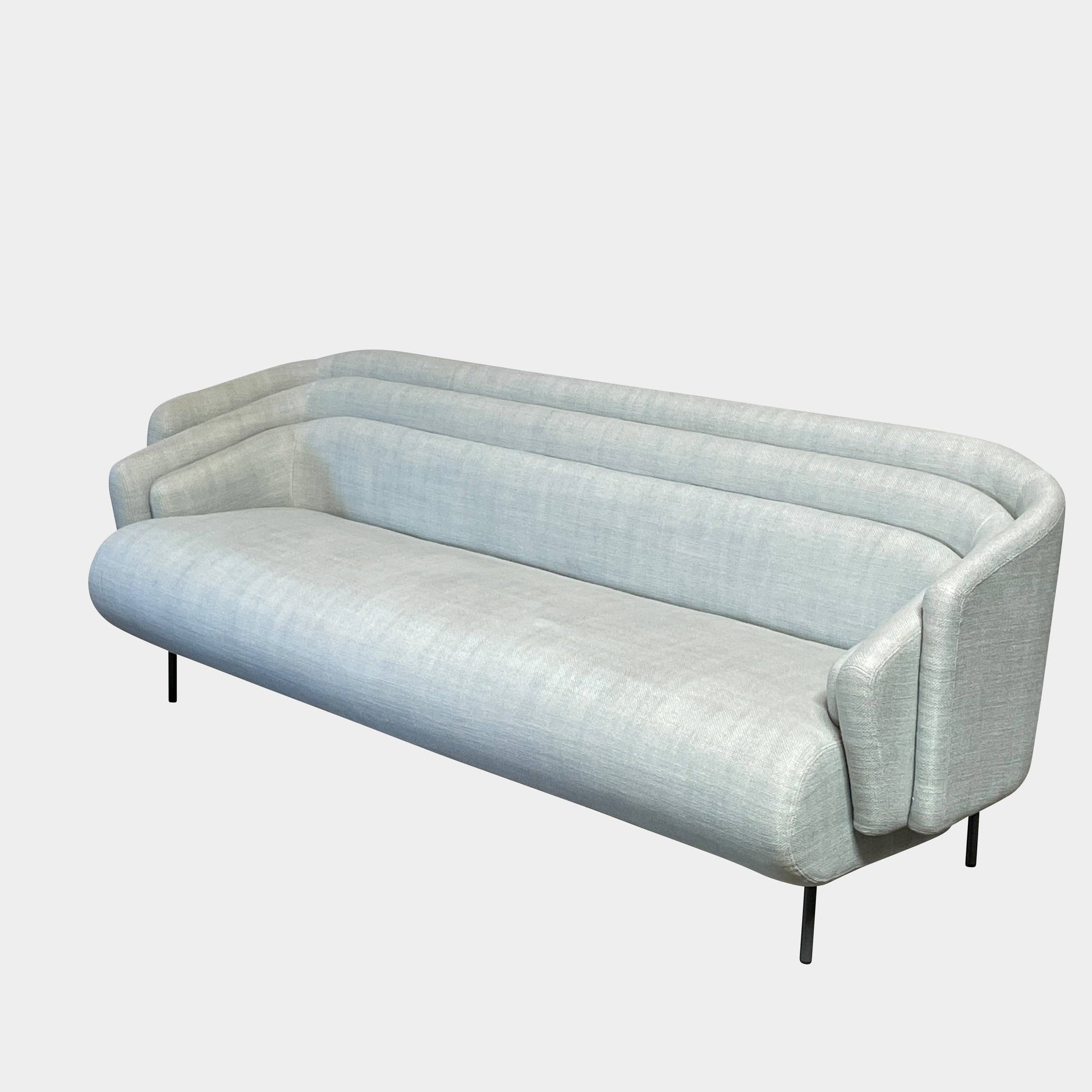 The Delcourt Collection Hug Sofa from the Delcourt Collection offers customizable fabric choices, including a light blue option, and is supported by sleek black legs.