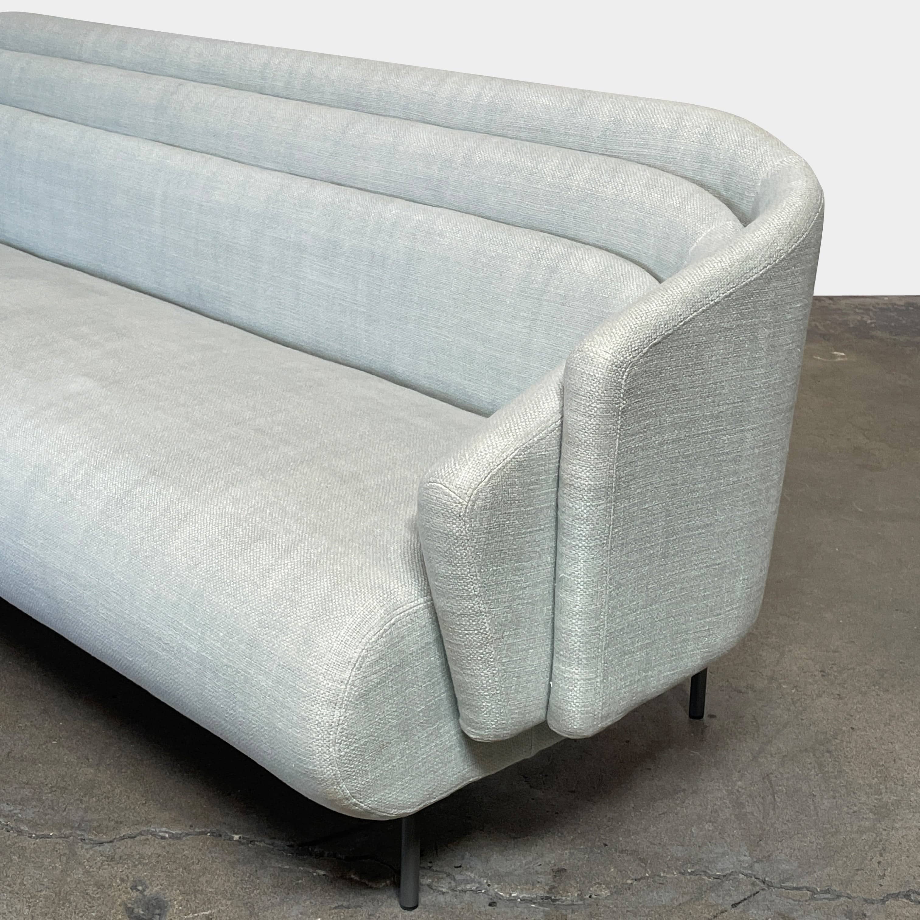 The Delcourt Collection Hug Sofa from the Delcourt Collection offers customizable fabric choices, including a light blue option, and is supported by sleek black legs.