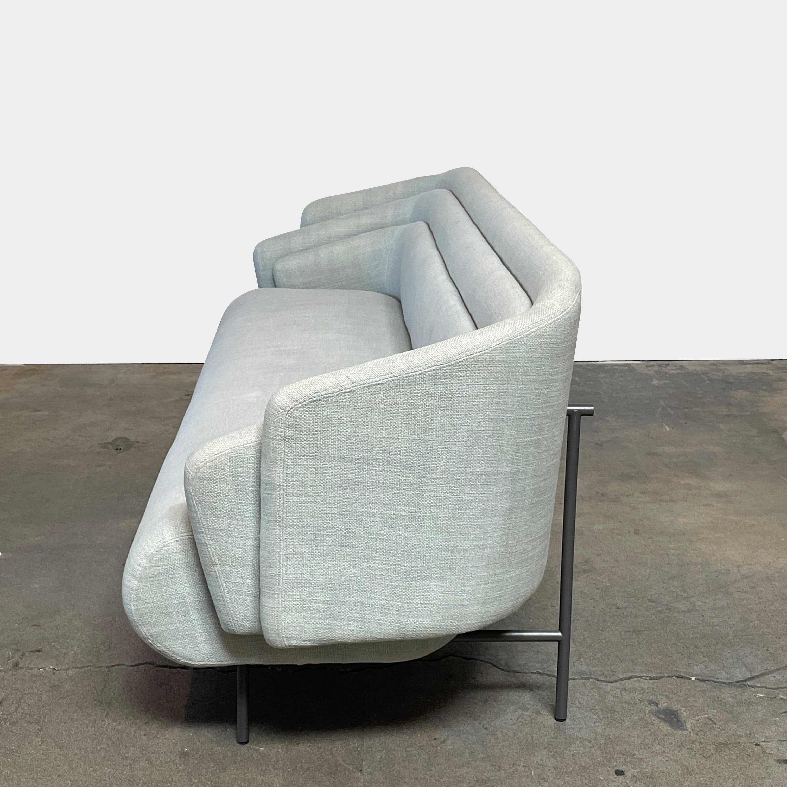 The Delcourt Collection Hug Sofa from the Delcourt Collection offers customizable fabric choices, including a light blue option, and is supported by sleek black legs.