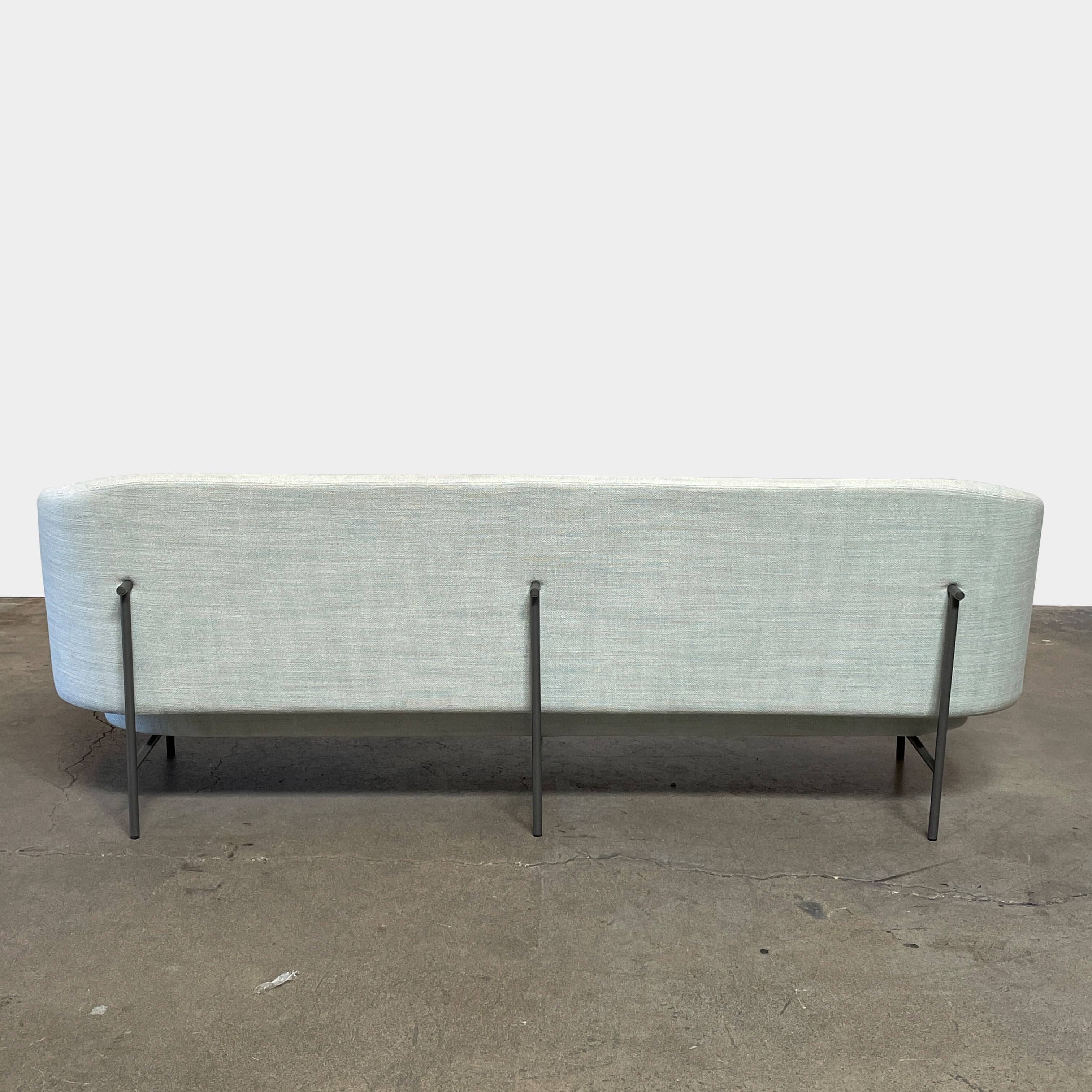 The Delcourt Collection Hug Sofa from the Delcourt Collection offers customizable fabric choices, including a light blue option, and is supported by sleek black legs.