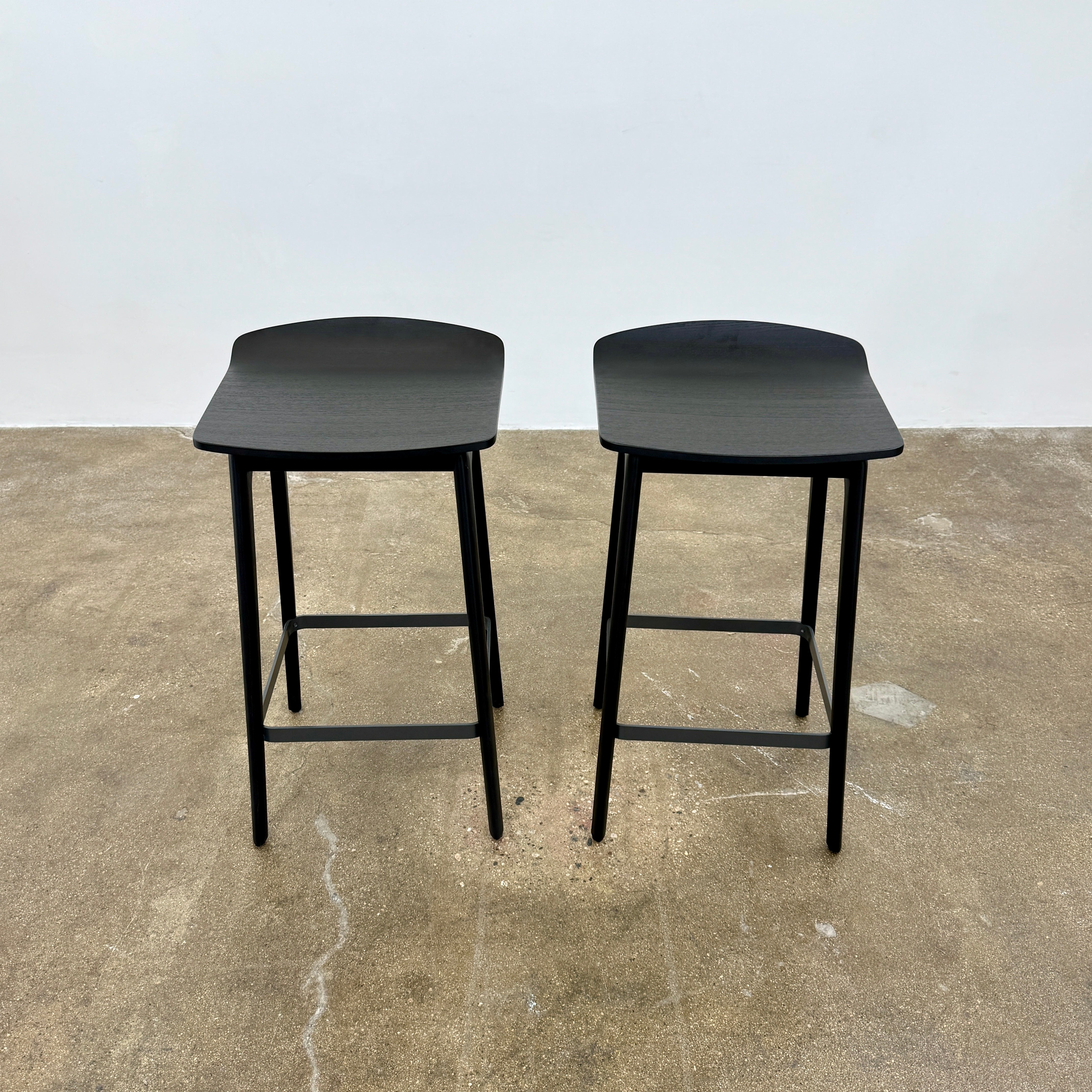 The Molteni & C Woody Kitchen Stool Set of 2 features black solid ash wood stools with curved seats and four legs, joined by support bars, shown on a plain white background.