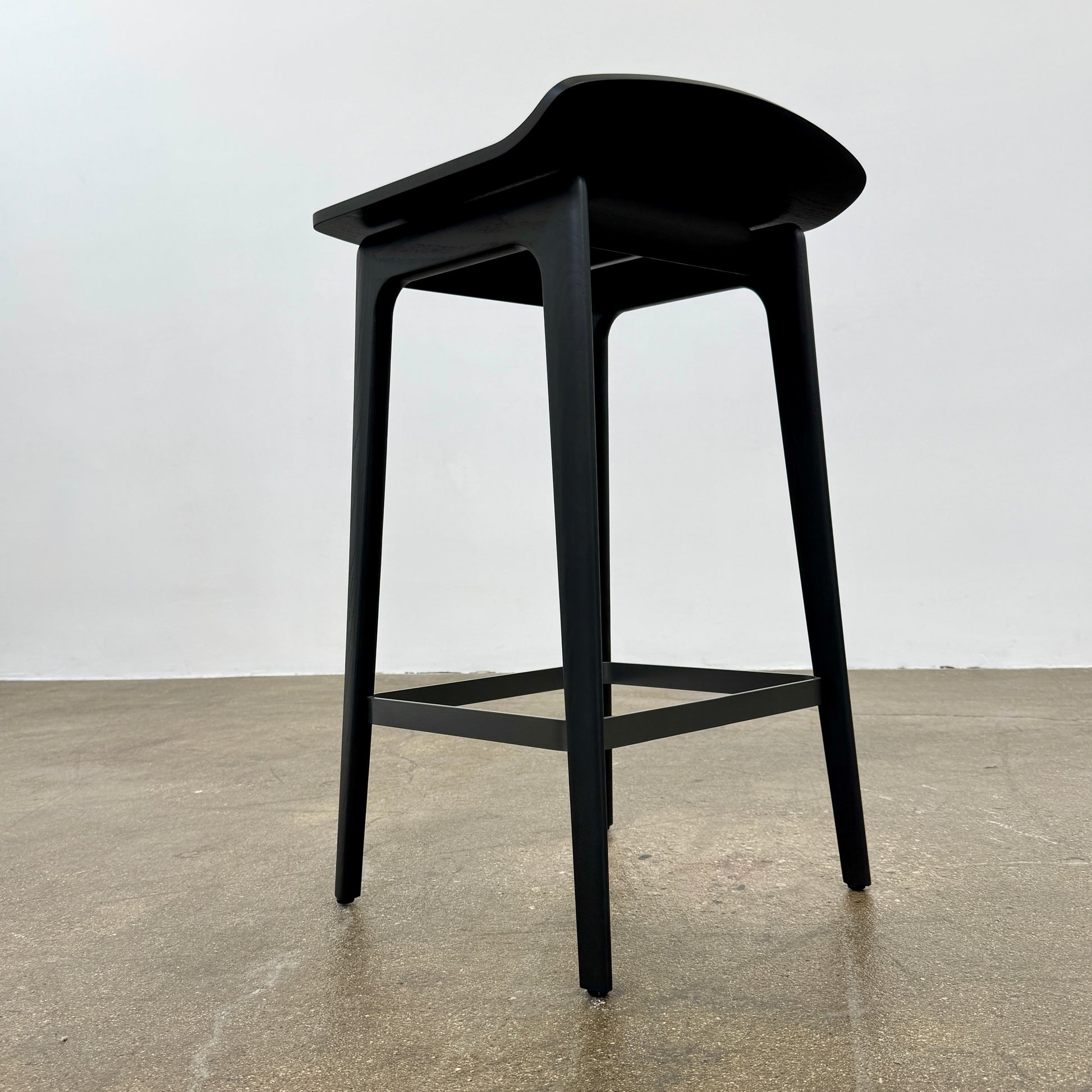 The Molteni & C Woody Kitchen Stool Set of 2 features black solid ash wood stools with curved seats and four legs, joined by support bars, shown on a plain white background.
