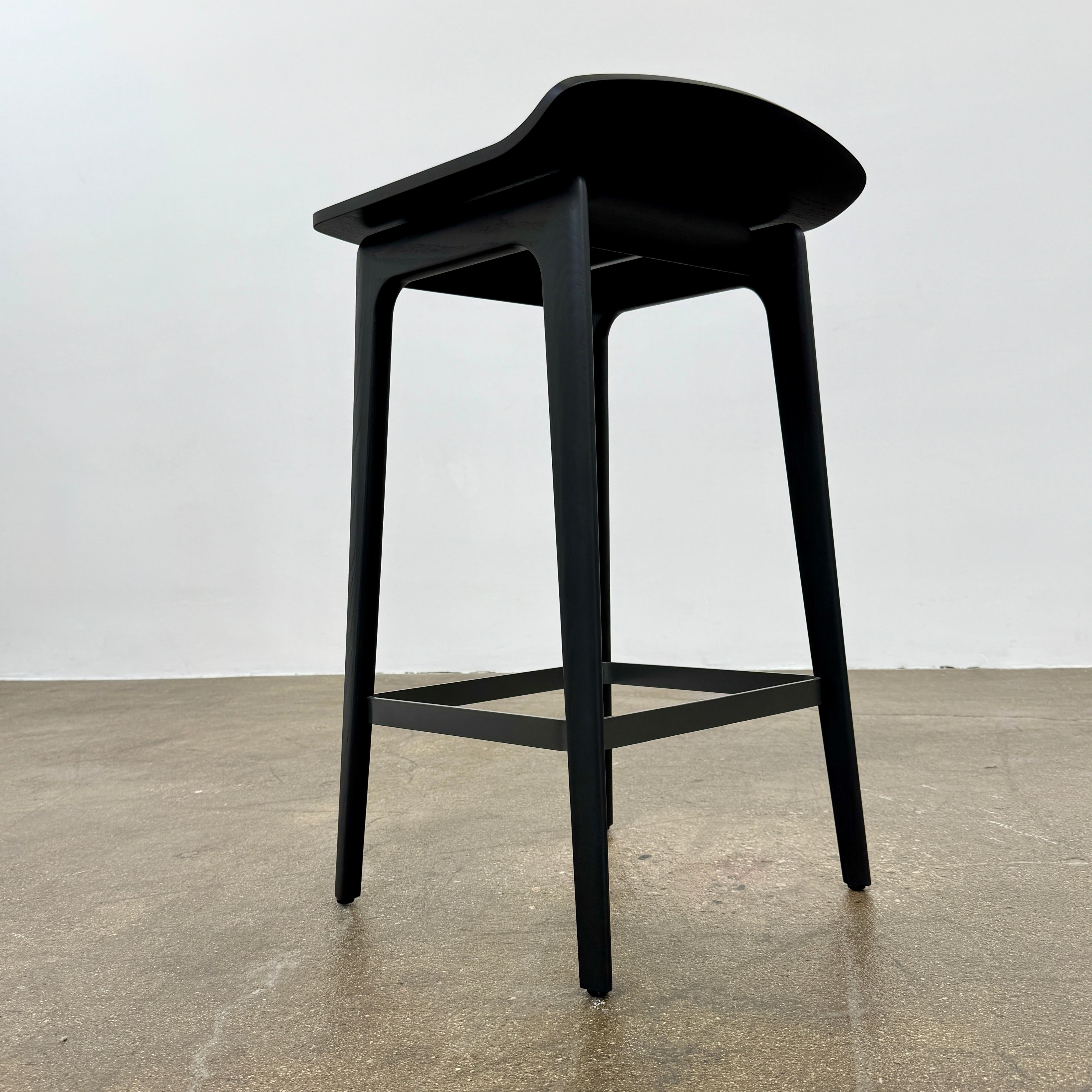 The Molteni & C Woody Kitchen Stool Set of 2 features black solid ash wood stools with curved seats and four legs, joined by support bars, shown on a plain white background.