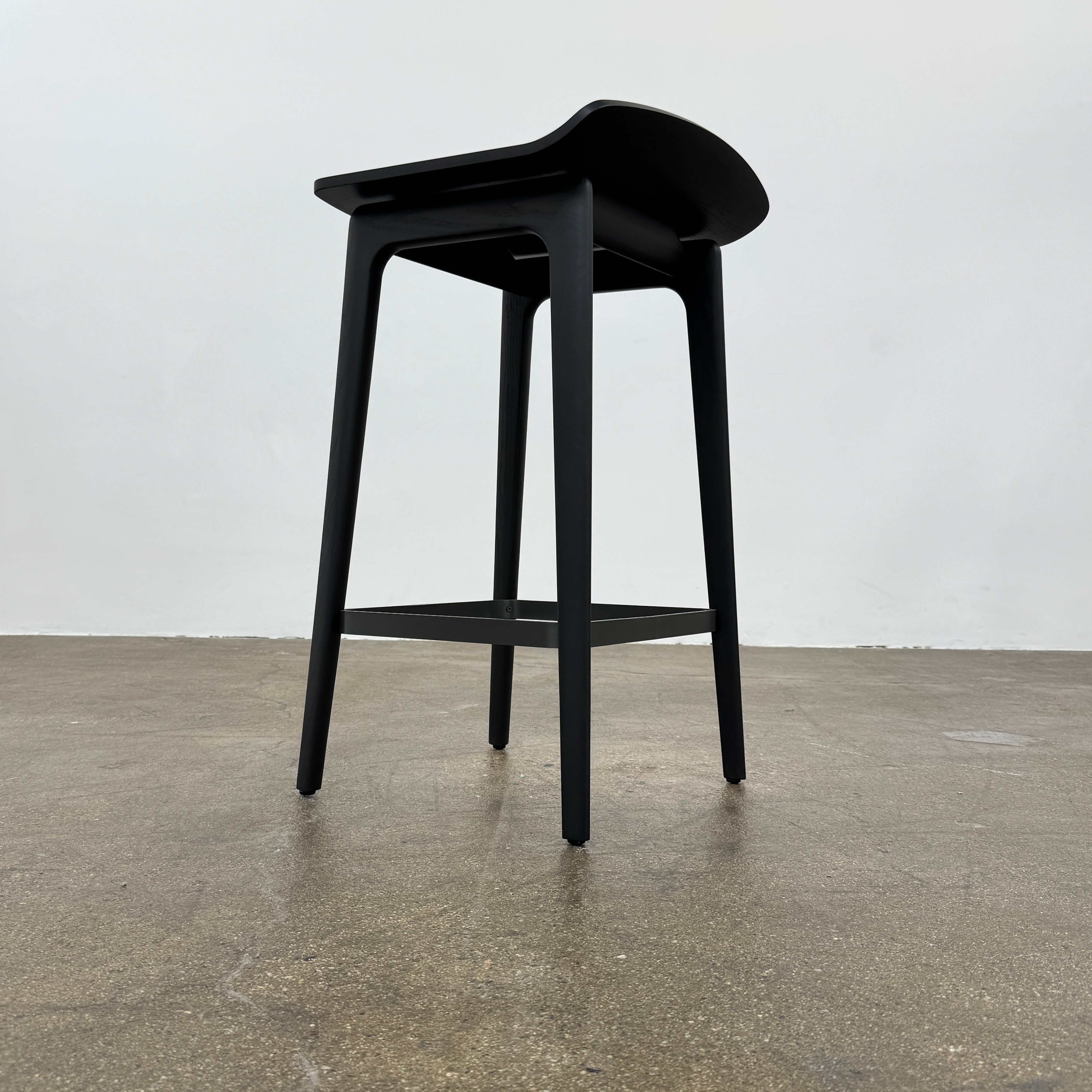 The Molteni & C Woody Kitchen Stool Set of 2 features black solid ash wood stools with curved seats and four legs, joined by support bars, shown on a plain white background.
