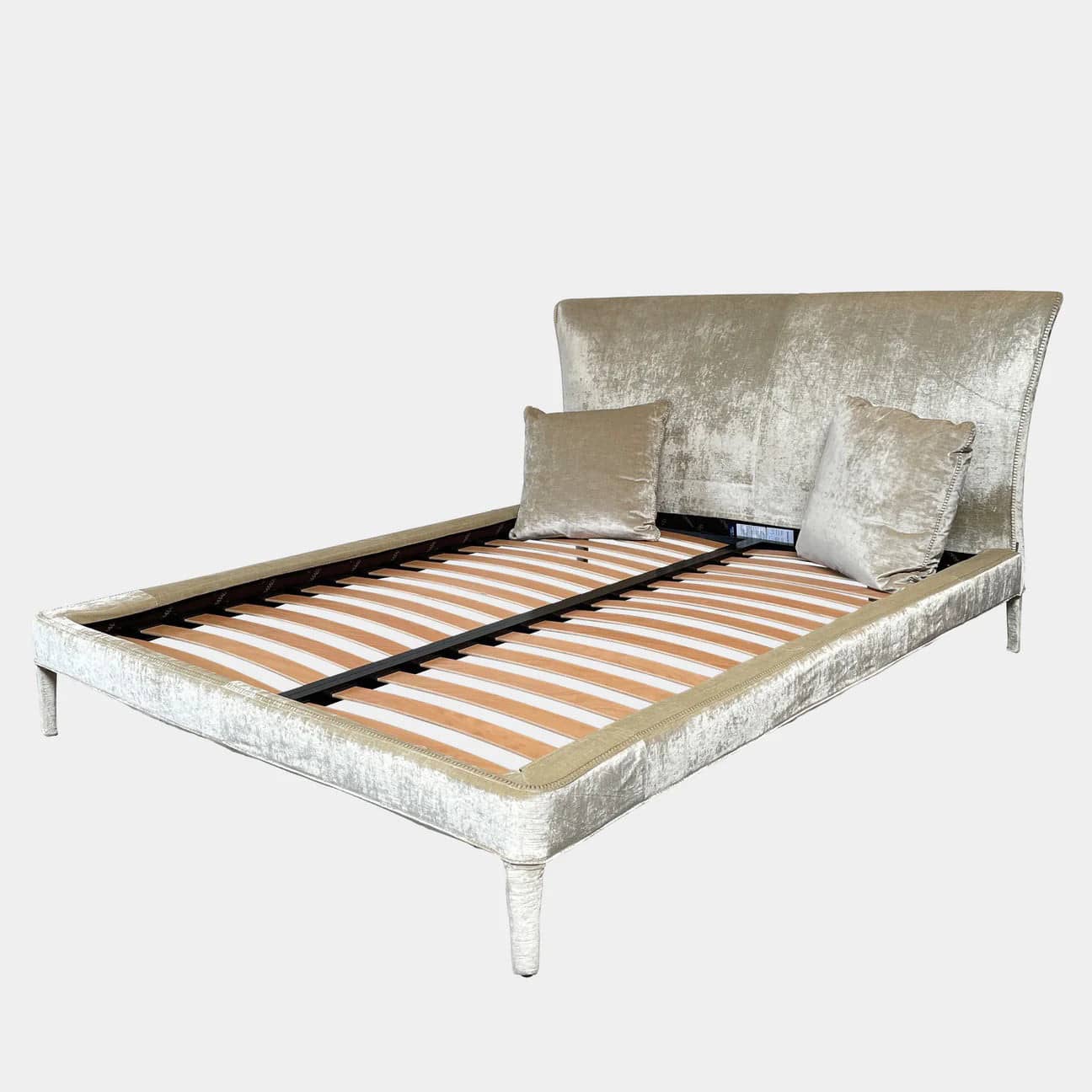 The Maxalto Febo Queen Bed is an upholstered bed frame featuring a headboard and two pillows, all elegantly wrapped in champagne-colored velvet. The frame boasts wooden slats for support, providing the refined touch of a luxury hotel bed. Shown without a mattress.