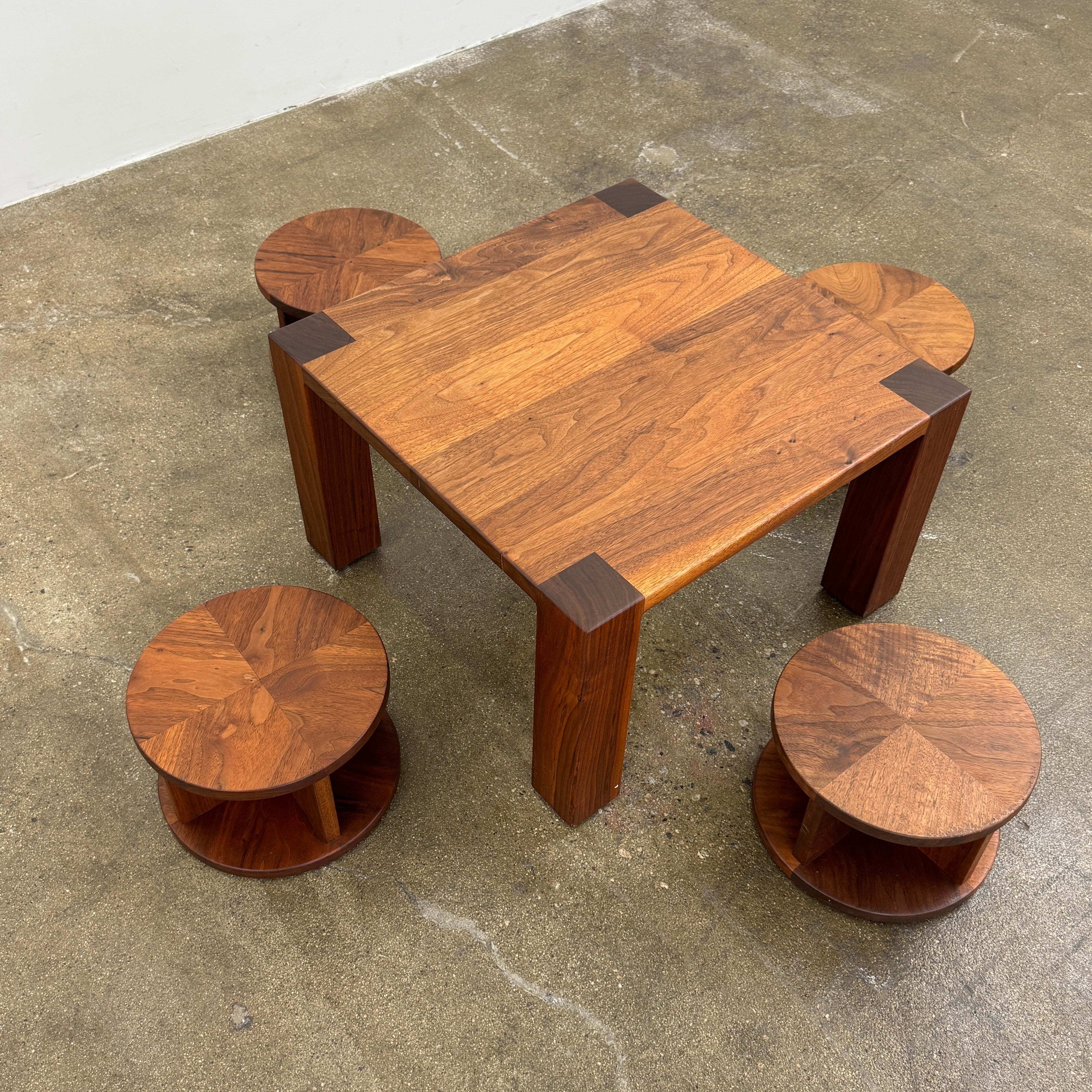 The Marmol Radziner Asher Children's Table and Stools features a square wooden table with four round stools fitting neatly underneath, all by Marmol Radziner, shown against a white background and inspired by their timeless design.