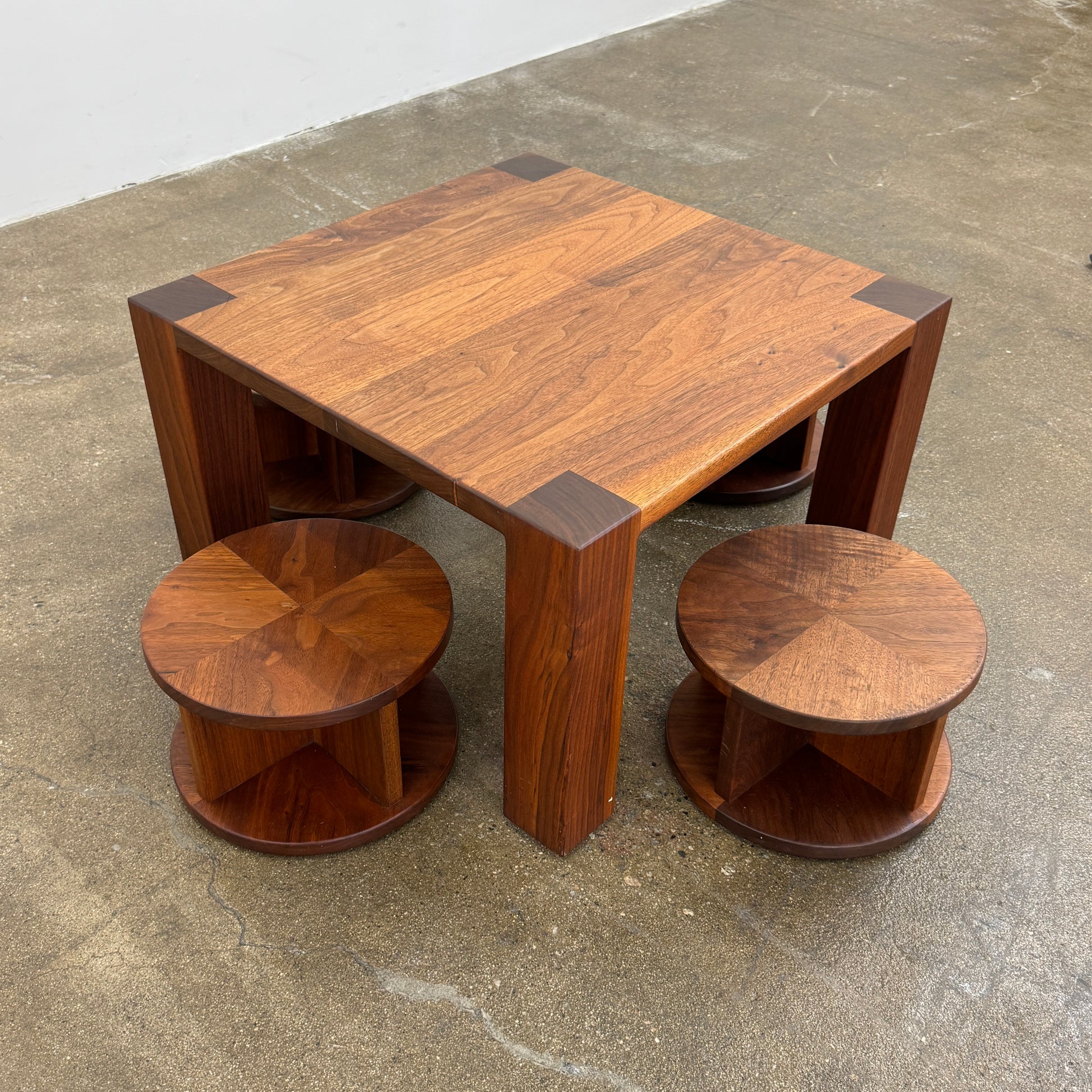 The Marmol Radziner Asher Children's Table and Stools features a square wooden table with four round stools fitting neatly underneath, all by Marmol Radziner, shown against a white background and inspired by their timeless design.