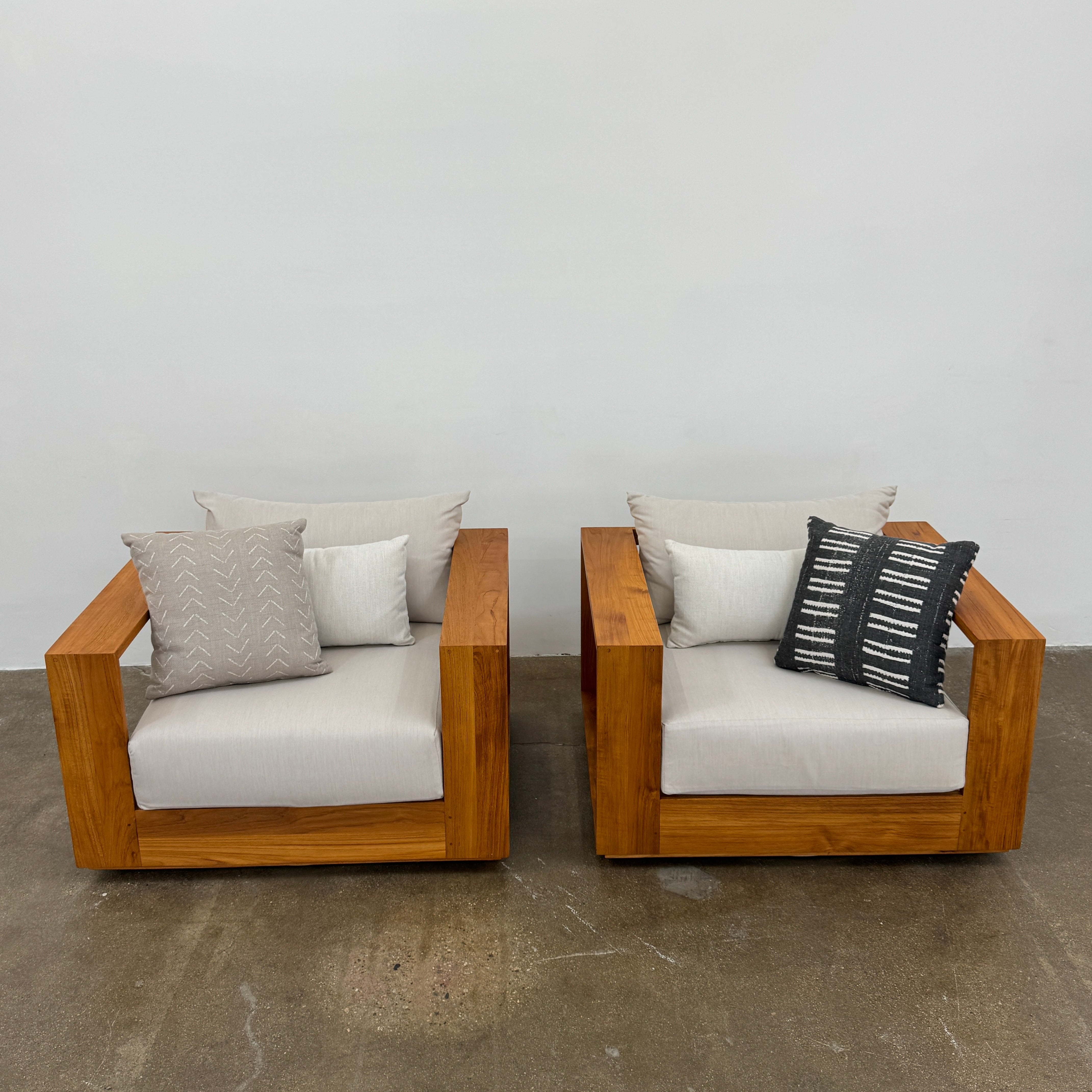 The Harbour Hayman Teak Outdoor Swivel Lounge Chair by Harbour features a modern design with a light beige cushion and a black-and-white patterned throw pillow, shown against a plain white background.