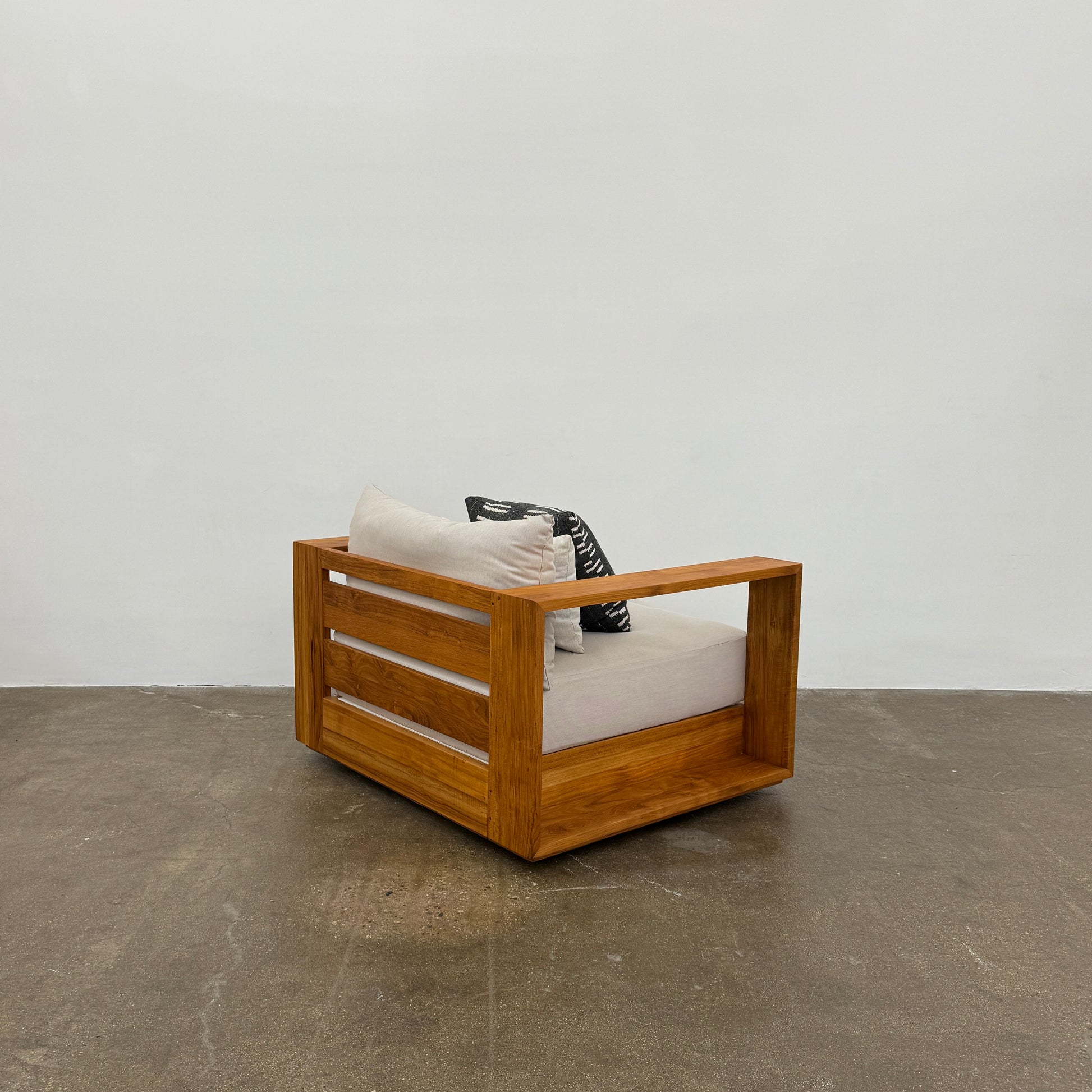 The Harbour Hayman Teak Outdoor Swivel Lounge Chair by Harbour features a modern design with a light beige cushion and a black-and-white patterned throw pillow, shown against a plain white background.