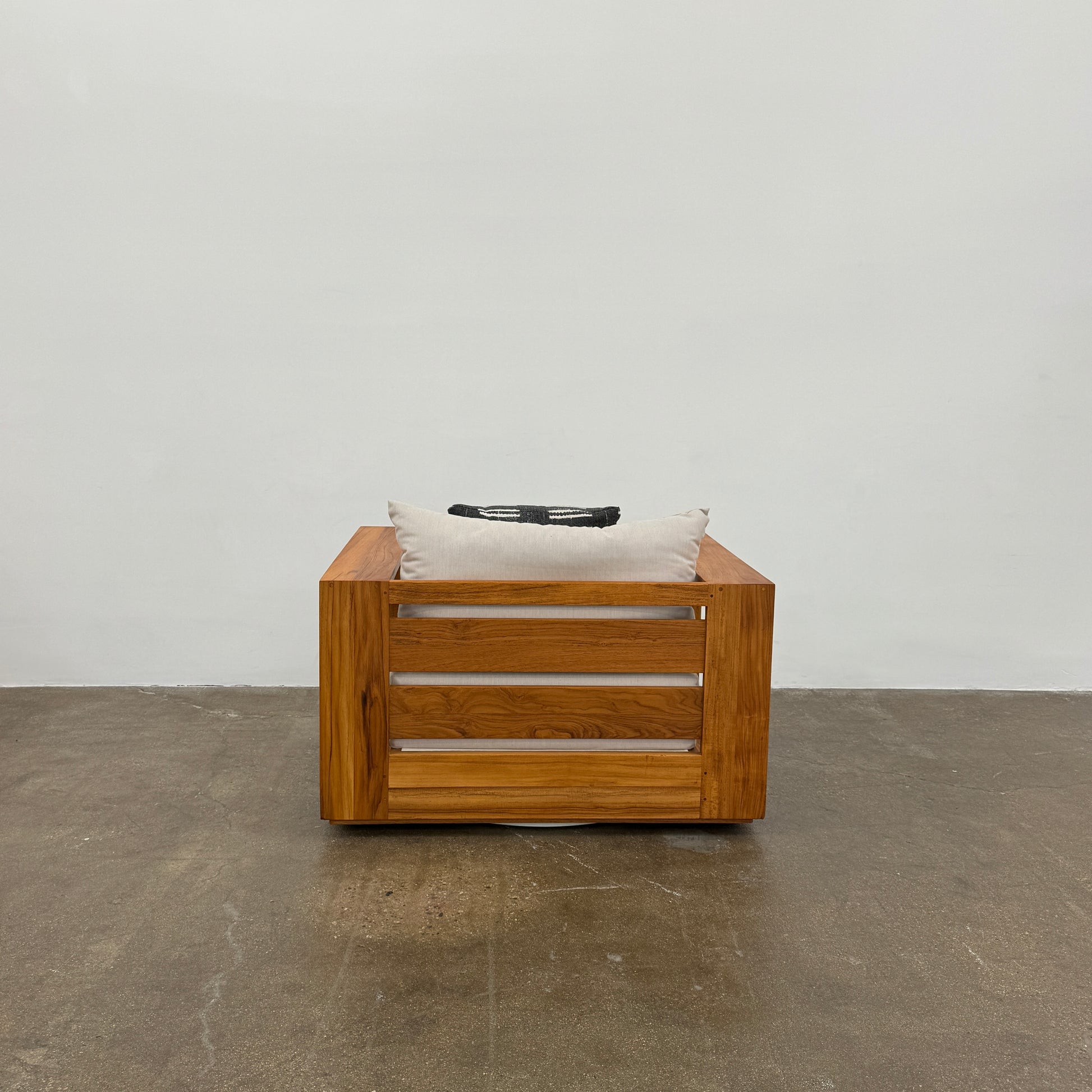 The Harbour Hayman Teak Outdoor Swivel Lounge Chair by Harbour features a modern design with a light beige cushion and a black-and-white patterned throw pillow, shown against a plain white background.