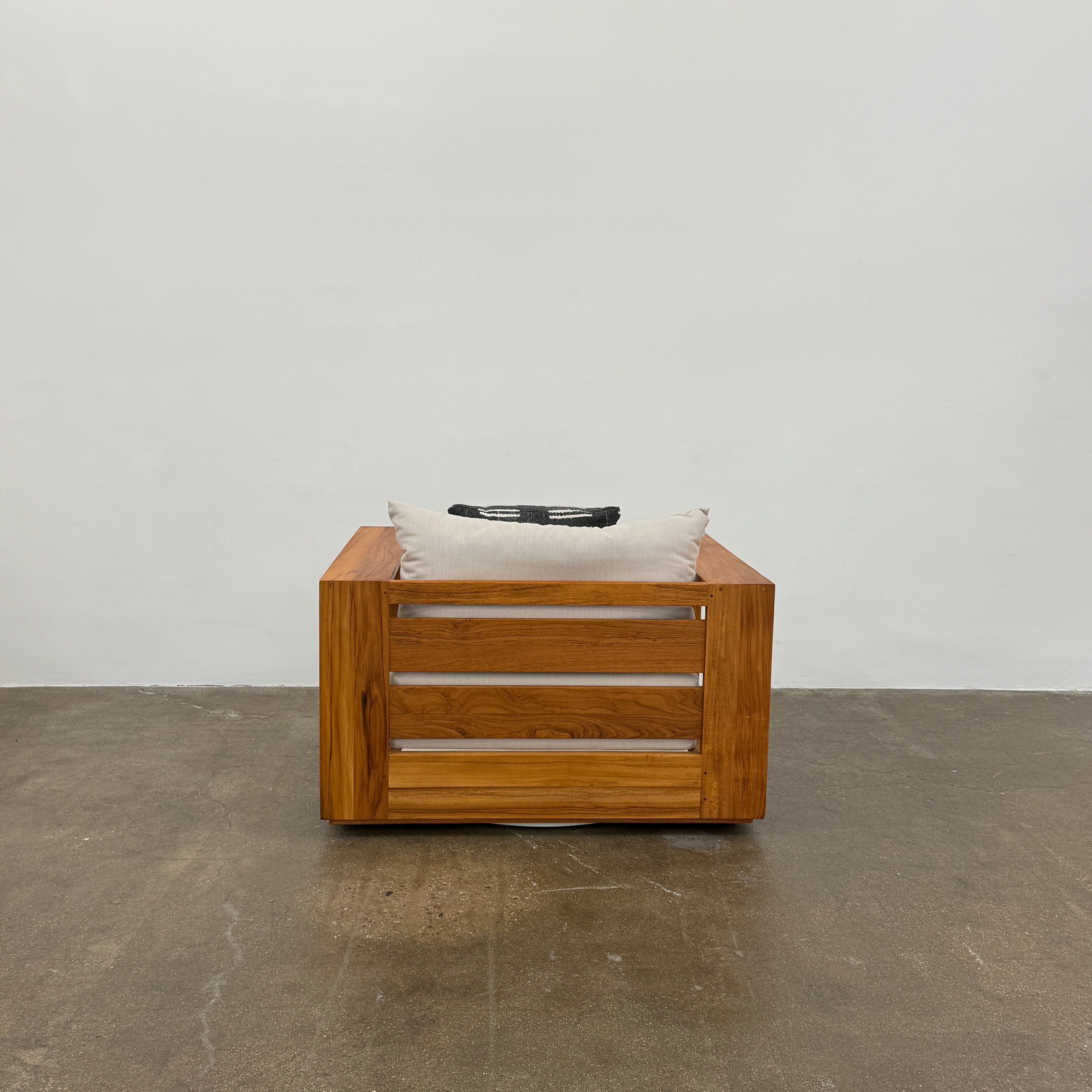 The Harbour Hayman Teak Outdoor Swivel Lounge Chair by Harbour features a modern design with a light beige cushion and a black-and-white patterned throw pillow, shown against a plain white background.