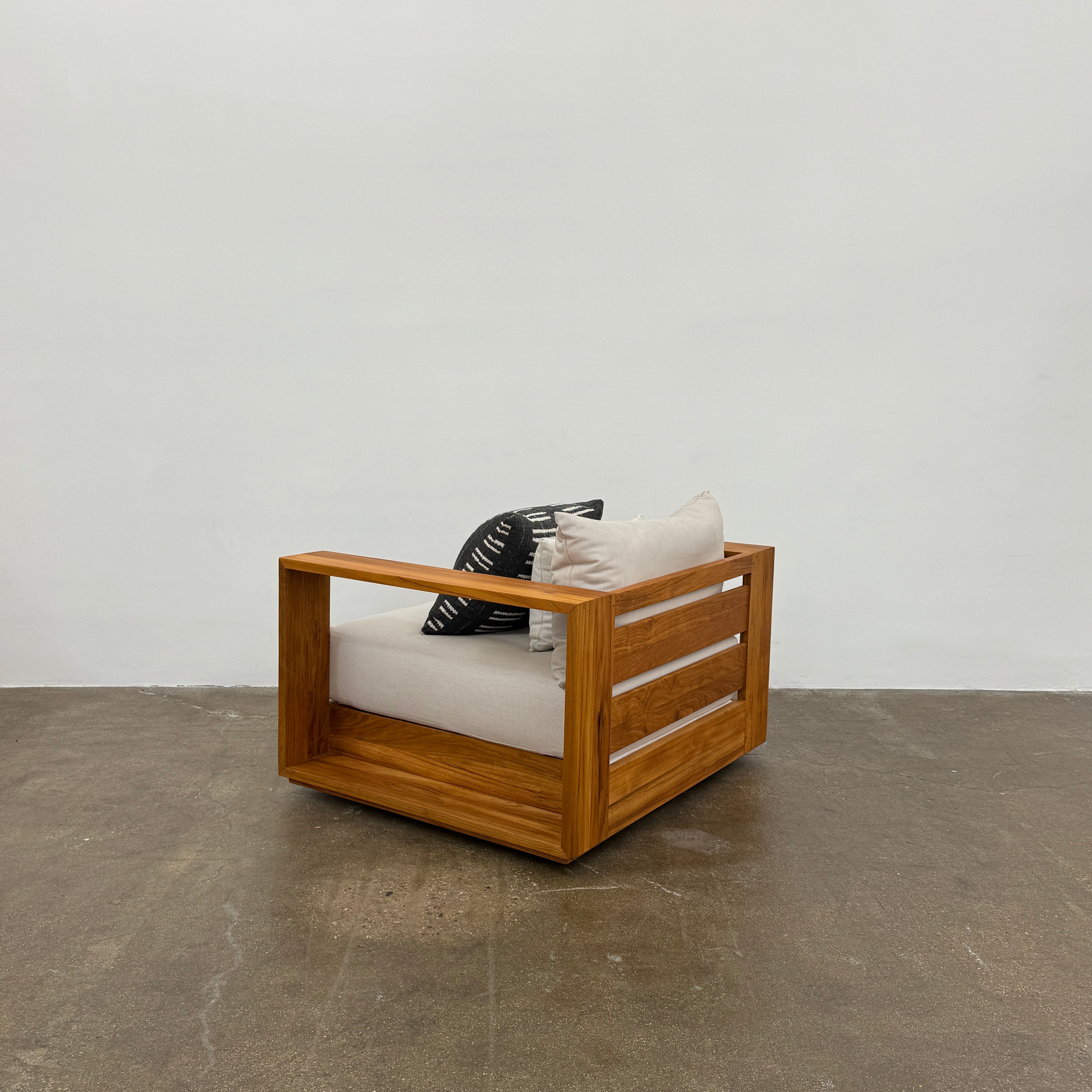 The Harbour Hayman Teak Outdoor Swivel Lounge Chair by Harbour features a modern design with a light beige cushion and a black-and-white patterned throw pillow, shown against a plain white background.