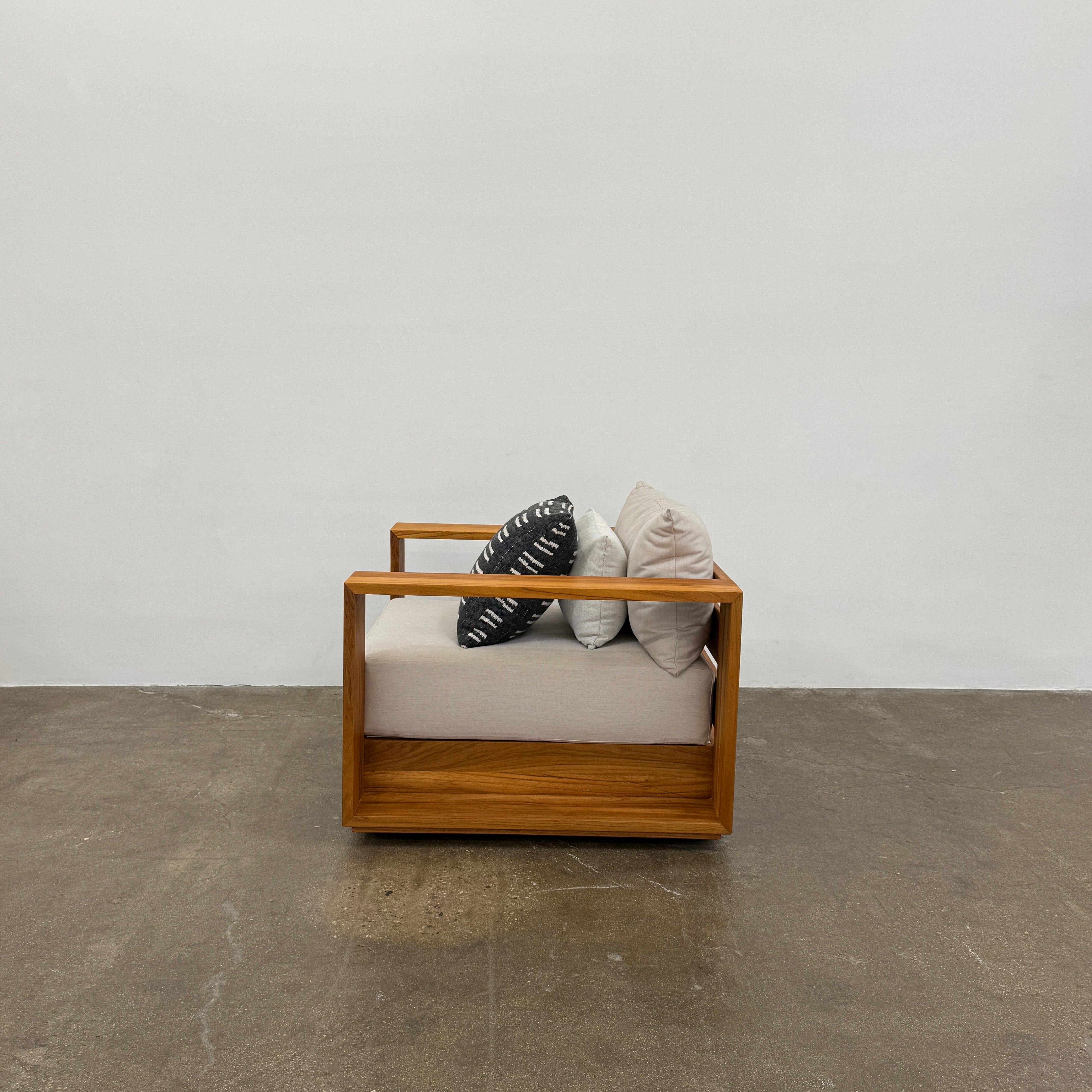 The Harbour Hayman Teak Outdoor Swivel Lounge Chair by Harbour features a modern design with a light beige cushion and a black-and-white patterned throw pillow, shown against a plain white background.