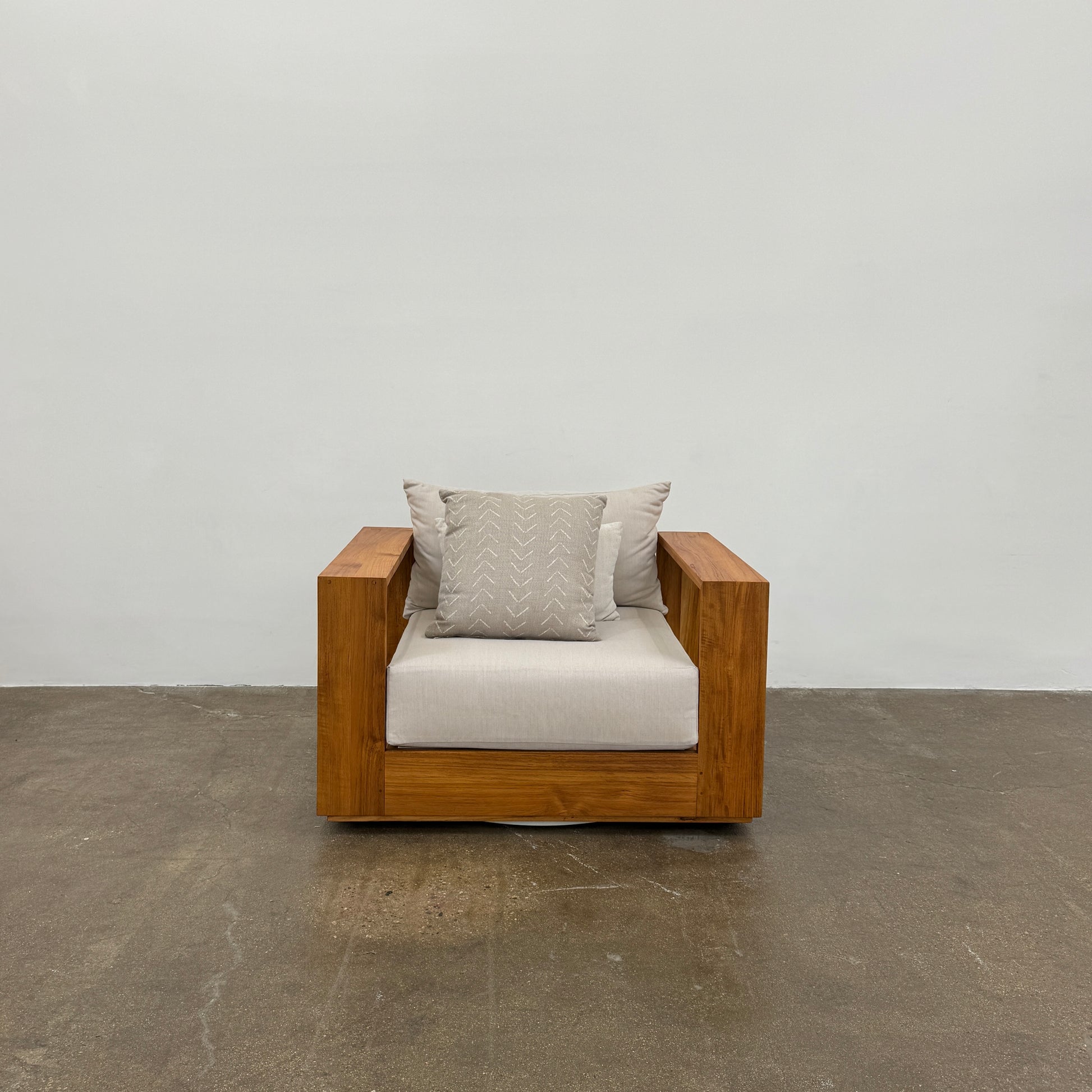 The Harbour Hayman Teak Outdoor Swivel Lounge Chair by Harbour features a modern design with a light beige cushion and a black-and-white patterned throw pillow, shown against a plain white background.