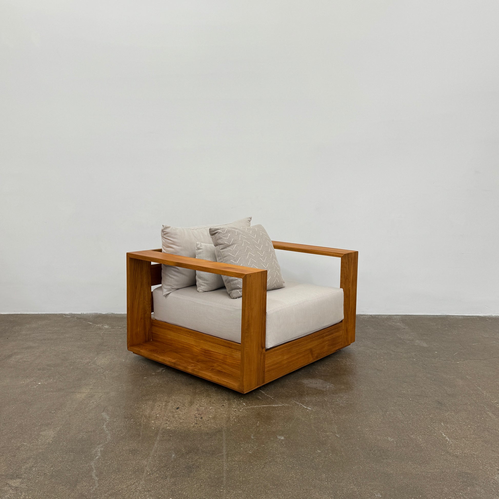 The Harbour Hayman Teak Outdoor Swivel Lounge Chair by Harbour features a modern design with a light beige cushion and a black-and-white patterned throw pillow, shown against a plain white background.