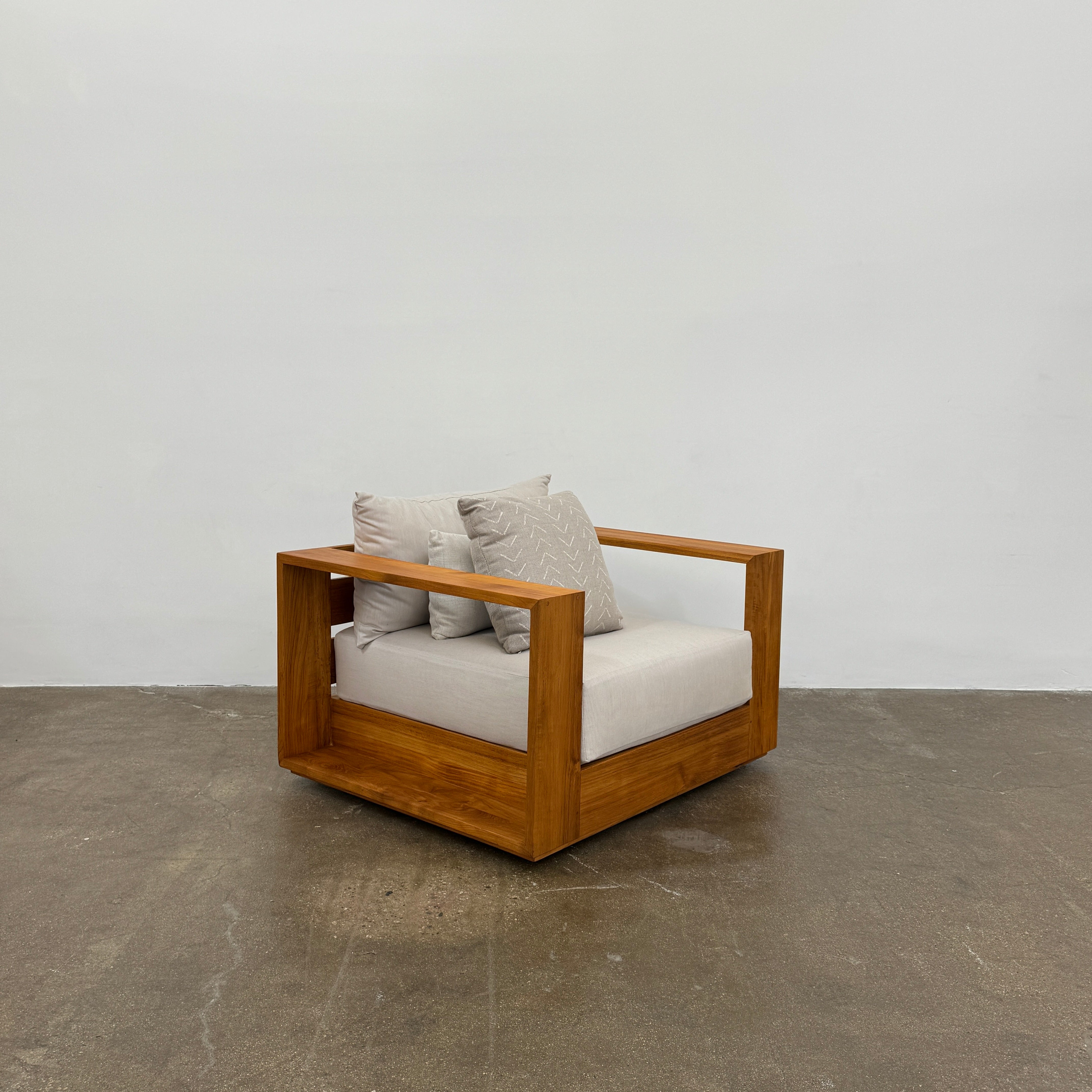 The Harbour Hayman Teak Outdoor Swivel Lounge Chair by Harbour features a modern design with a light beige cushion and a black-and-white patterned throw pillow, shown against a plain white background.