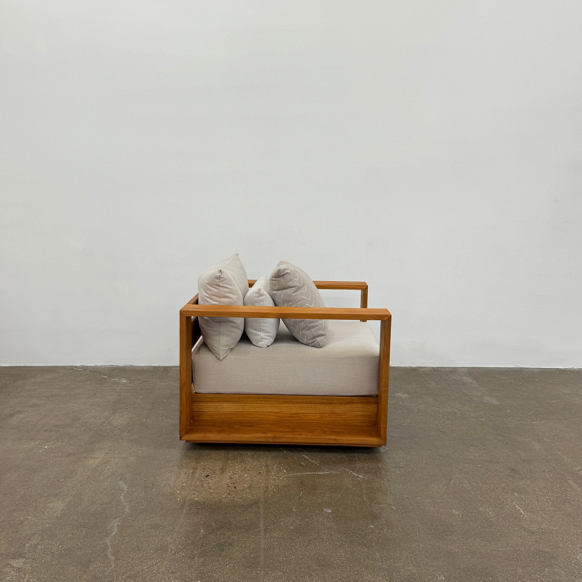 The Harbour Hayman Teak Outdoor Swivel Lounge Chair by Harbour features a modern design with a light beige cushion and a black-and-white patterned throw pillow, shown against a plain white background.