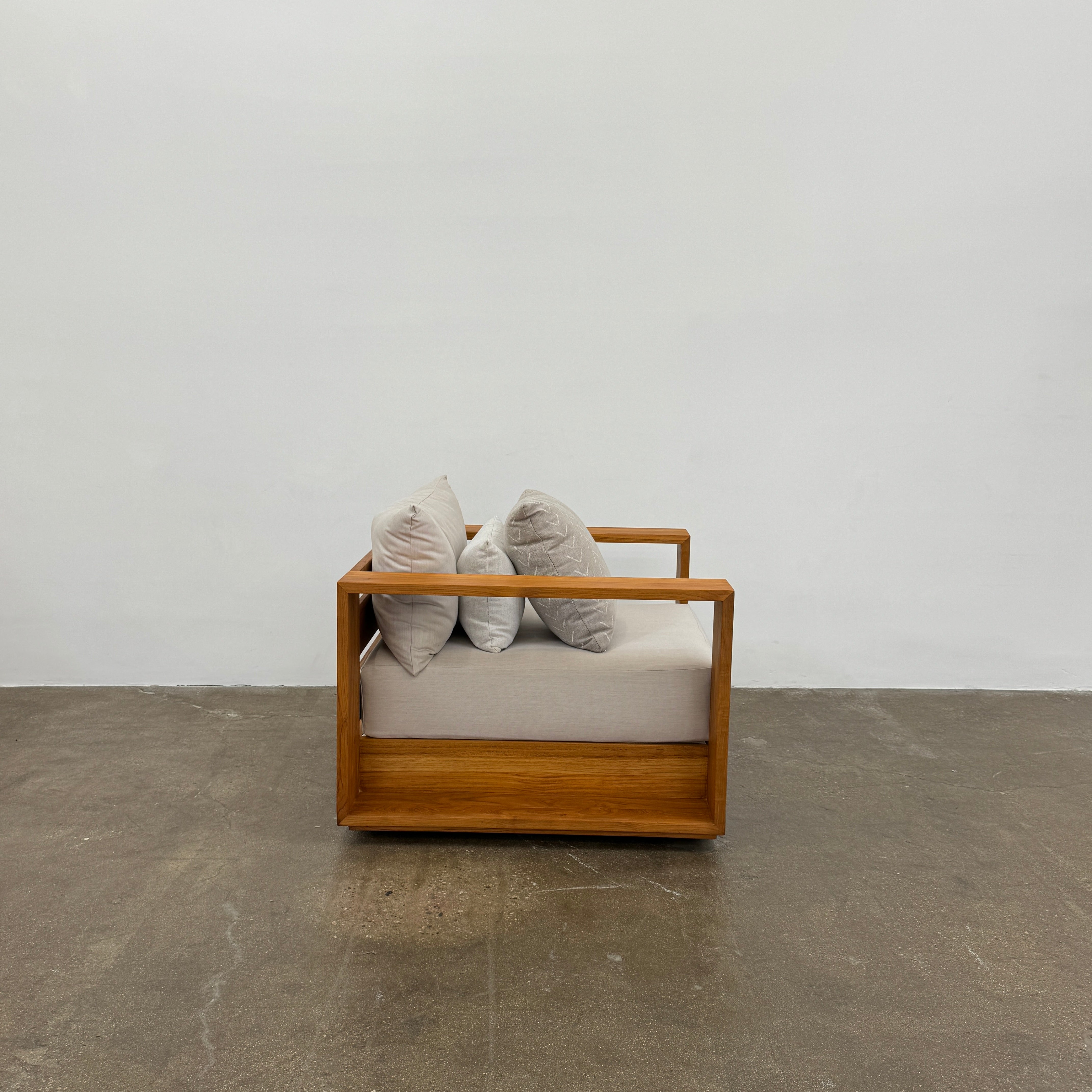 The Harbour Hayman Teak Outdoor Swivel Lounge Chair by Harbour features a modern design with a light beige cushion and a black-and-white patterned throw pillow, shown against a plain white background.