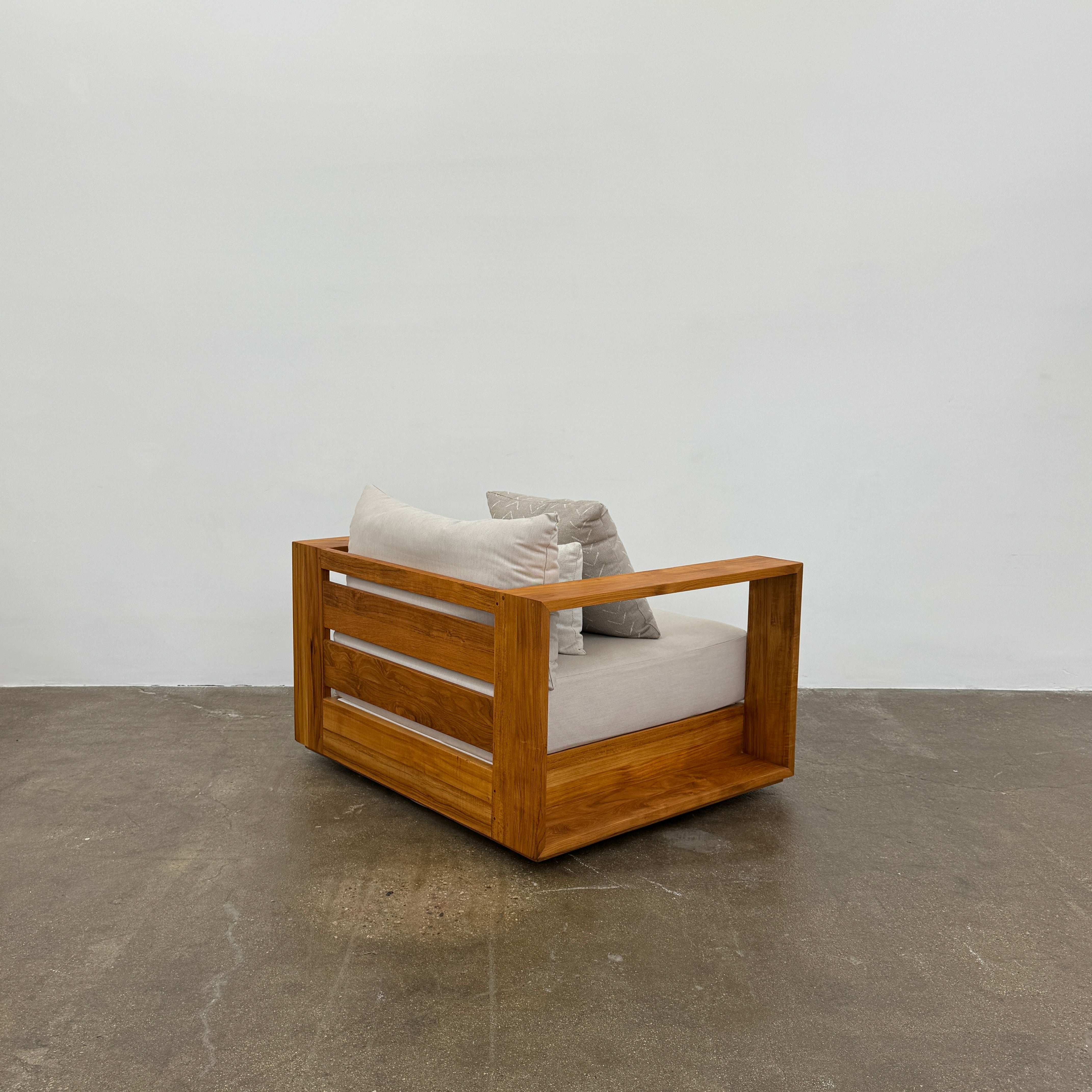 The Harbour Hayman Teak Outdoor Swivel Lounge Chair by Harbour features a modern design with a light beige cushion and a black-and-white patterned throw pillow, shown against a plain white background.