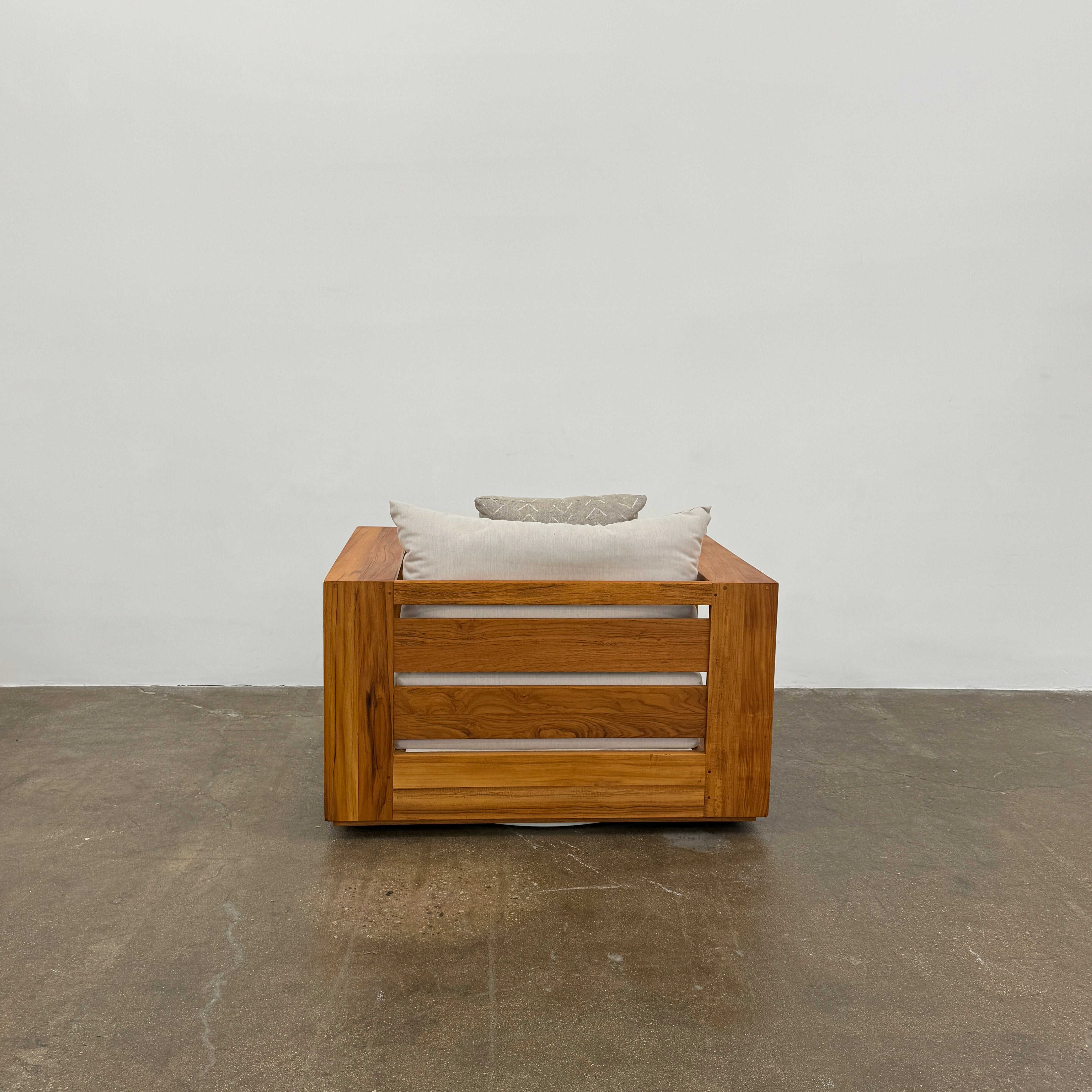 The Harbour Hayman Teak Outdoor Swivel Lounge Chair by Harbour features a modern design with a light beige cushion and a black-and-white patterned throw pillow, shown against a plain white background.