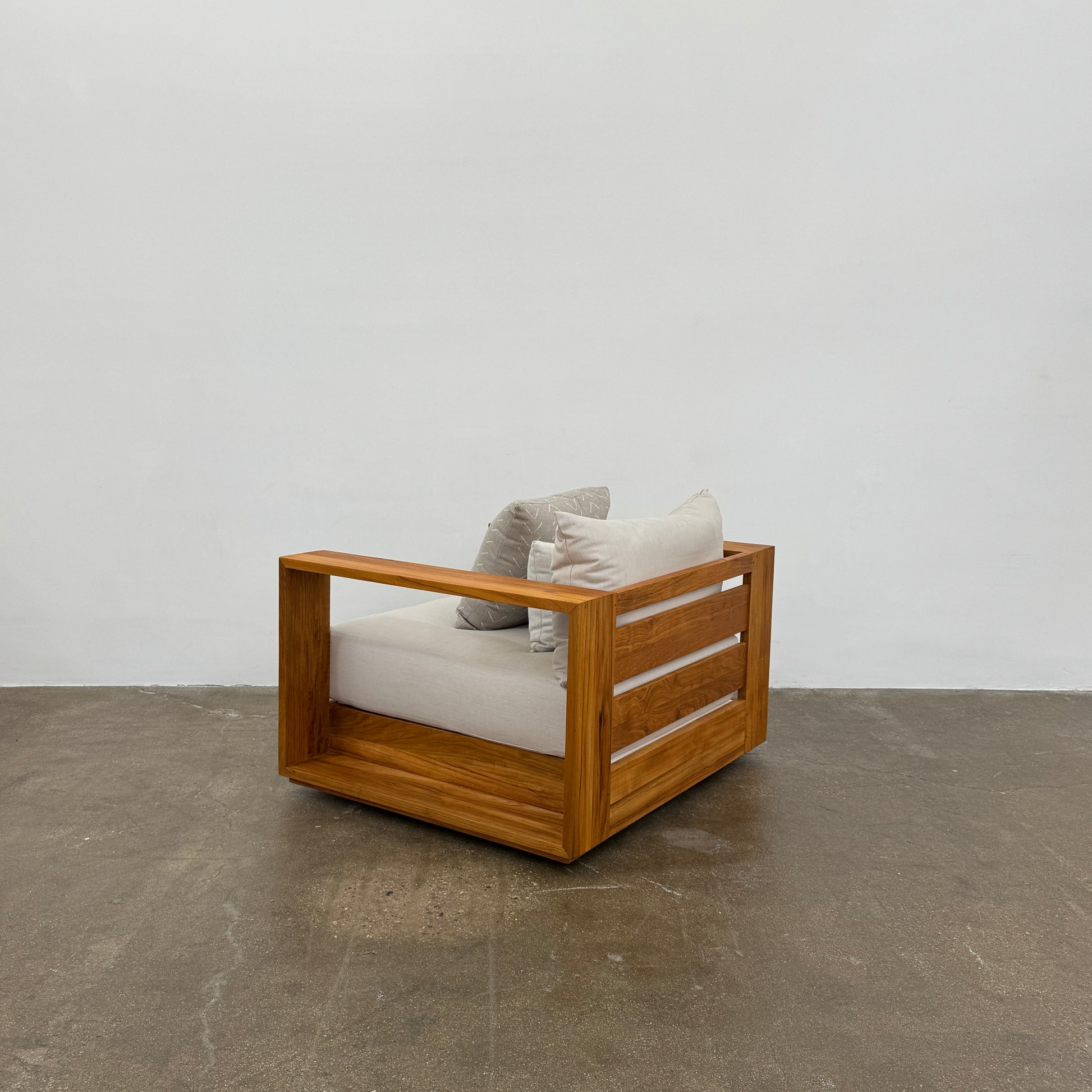 The Harbour Hayman Teak Outdoor Swivel Lounge Chair by Harbour features a modern design with a light beige cushion and a black-and-white patterned throw pillow, shown against a plain white background.