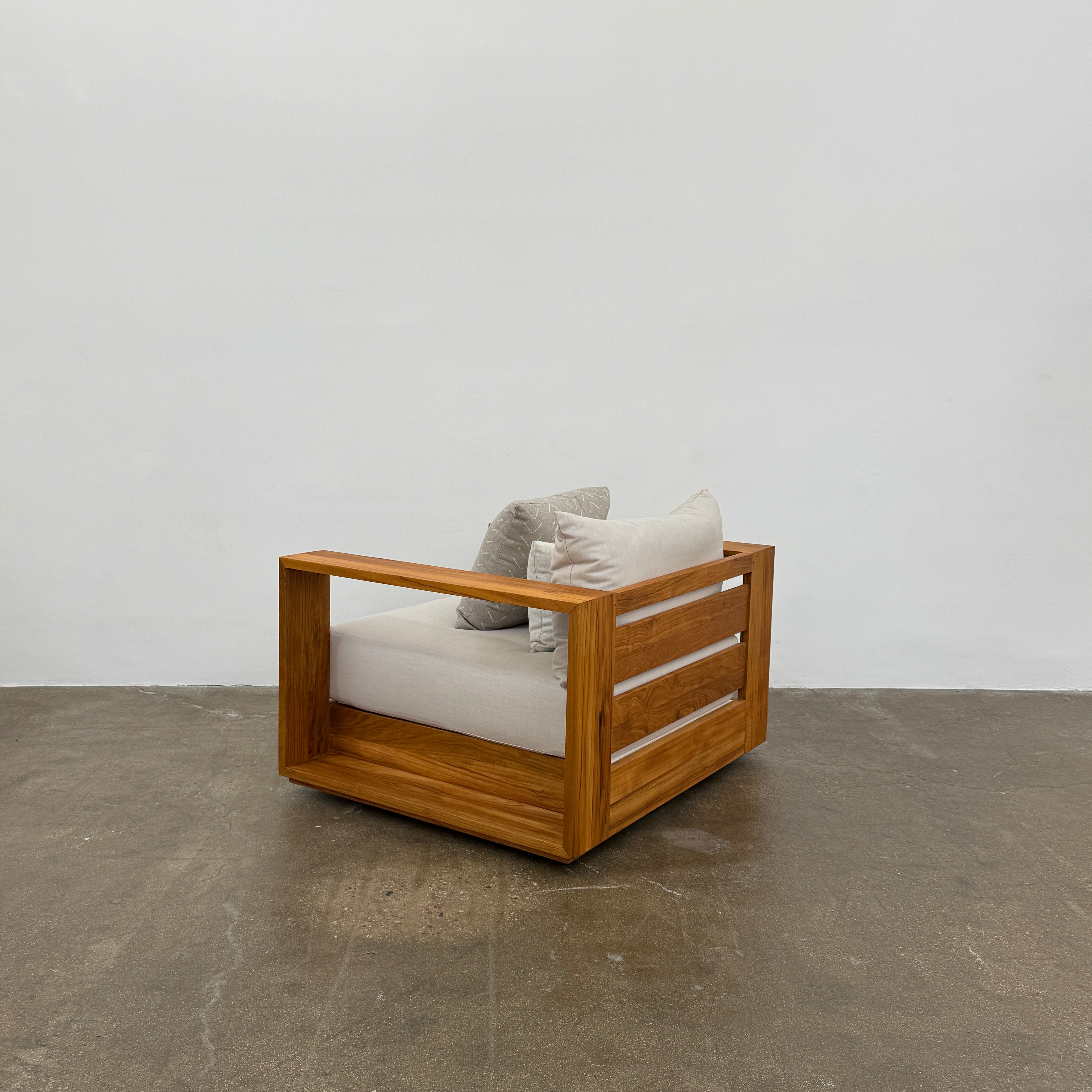 The Harbour Hayman Teak Outdoor Swivel Lounge Chair by Harbour features a modern design with a light beige cushion and a black-and-white patterned throw pillow, shown against a plain white background.