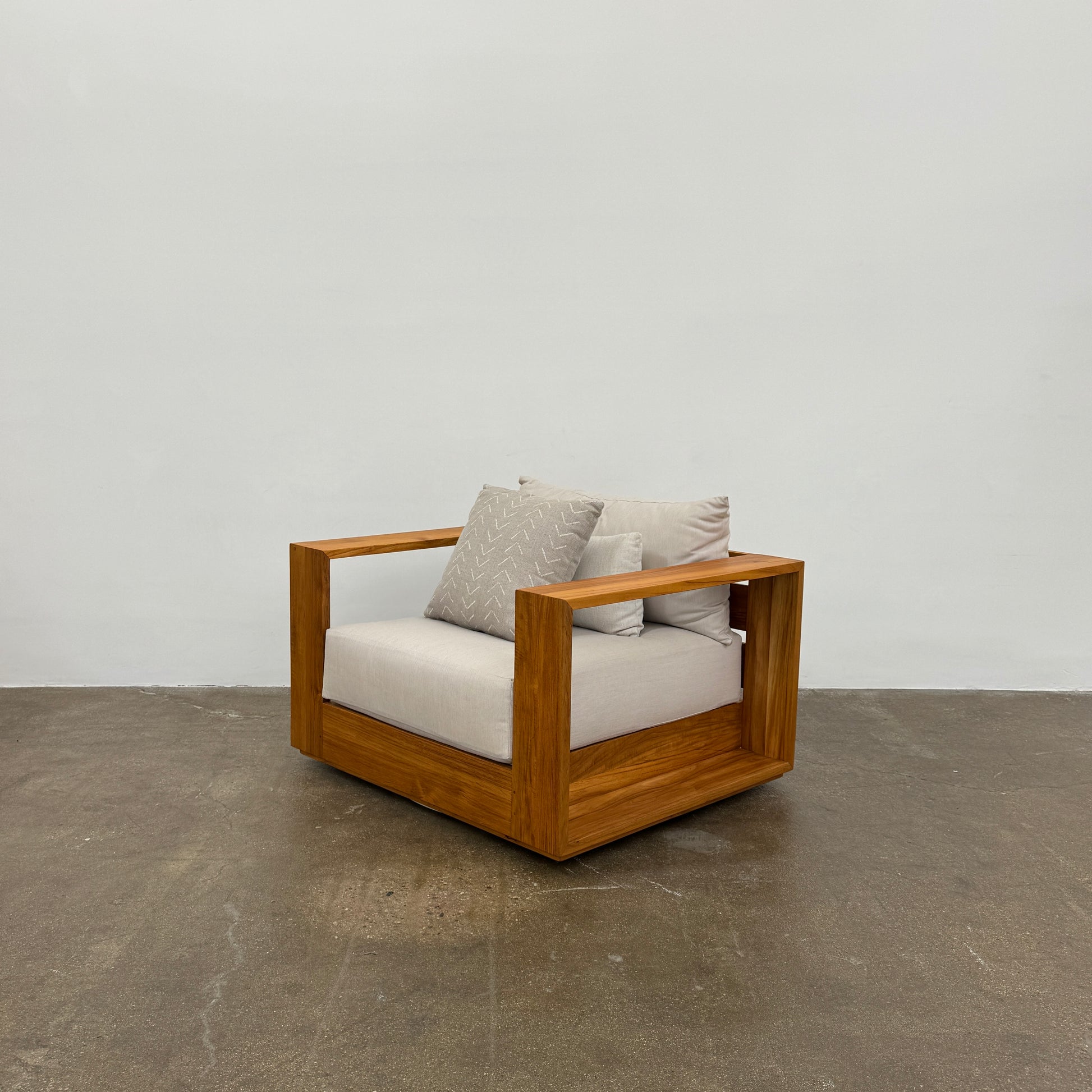 The Harbour Hayman Teak Outdoor Swivel Lounge Chair by Harbour features a modern design with a light beige cushion and a black-and-white patterned throw pillow, shown against a plain white background.