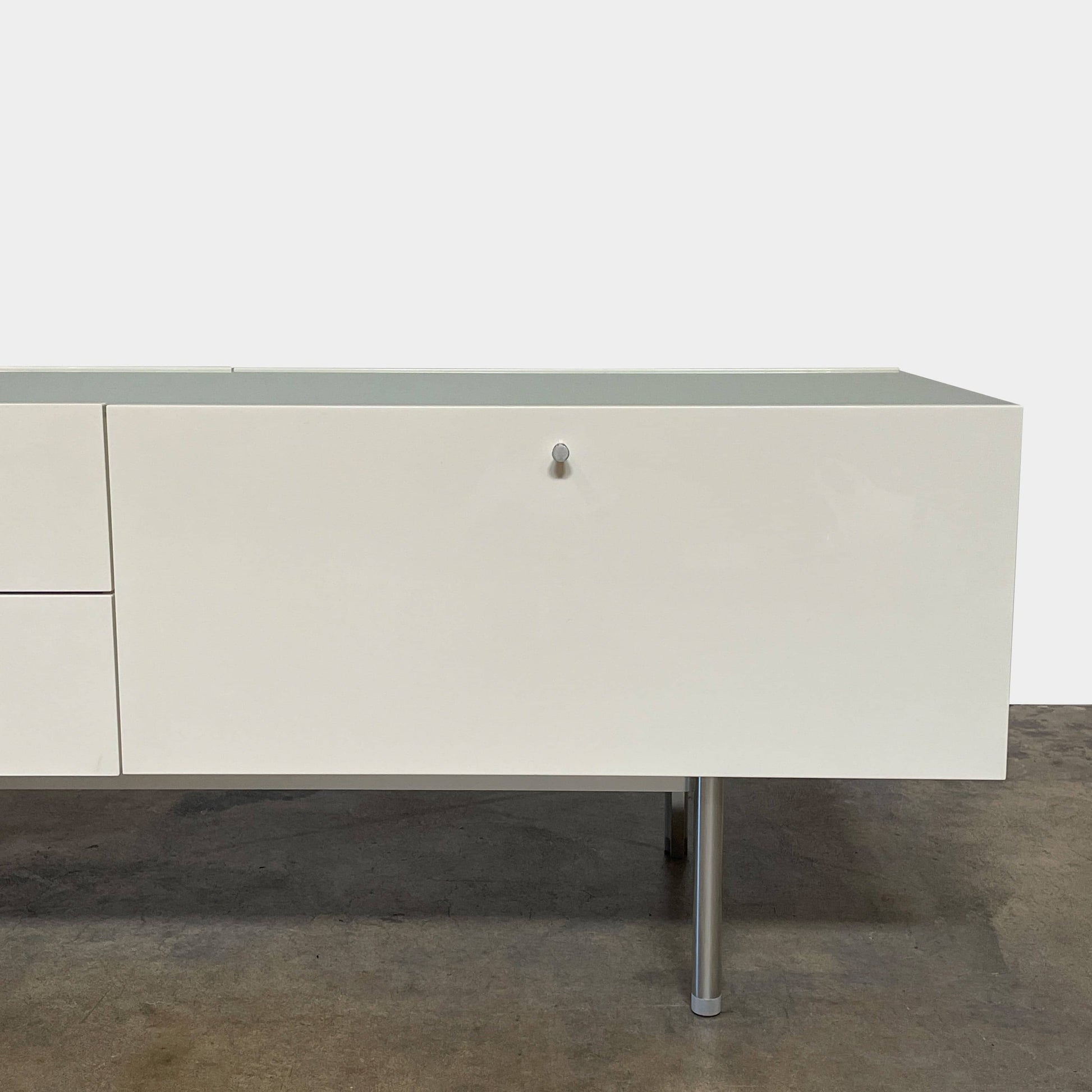 The Cassina 255-256 Flat Sideboard in glossy white lacquer features two left drawers, a spacious right compartment, and four metal legs, all by Cassina, shown against a plain background.
