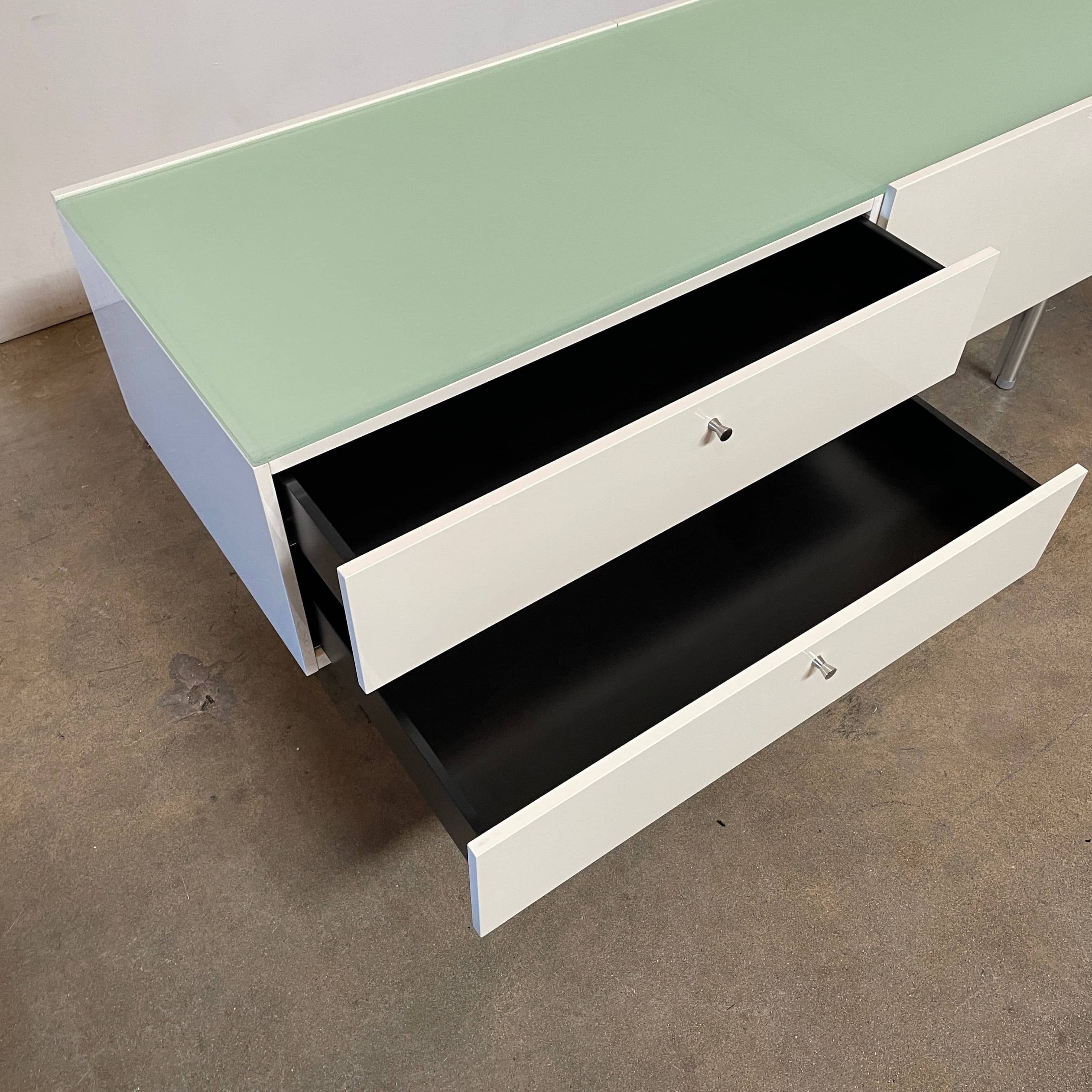 The Cassina 255-256 Flat Sideboard in glossy white lacquer features two left drawers, a spacious right compartment, and four metal legs, all by Cassina, shown against a plain background.