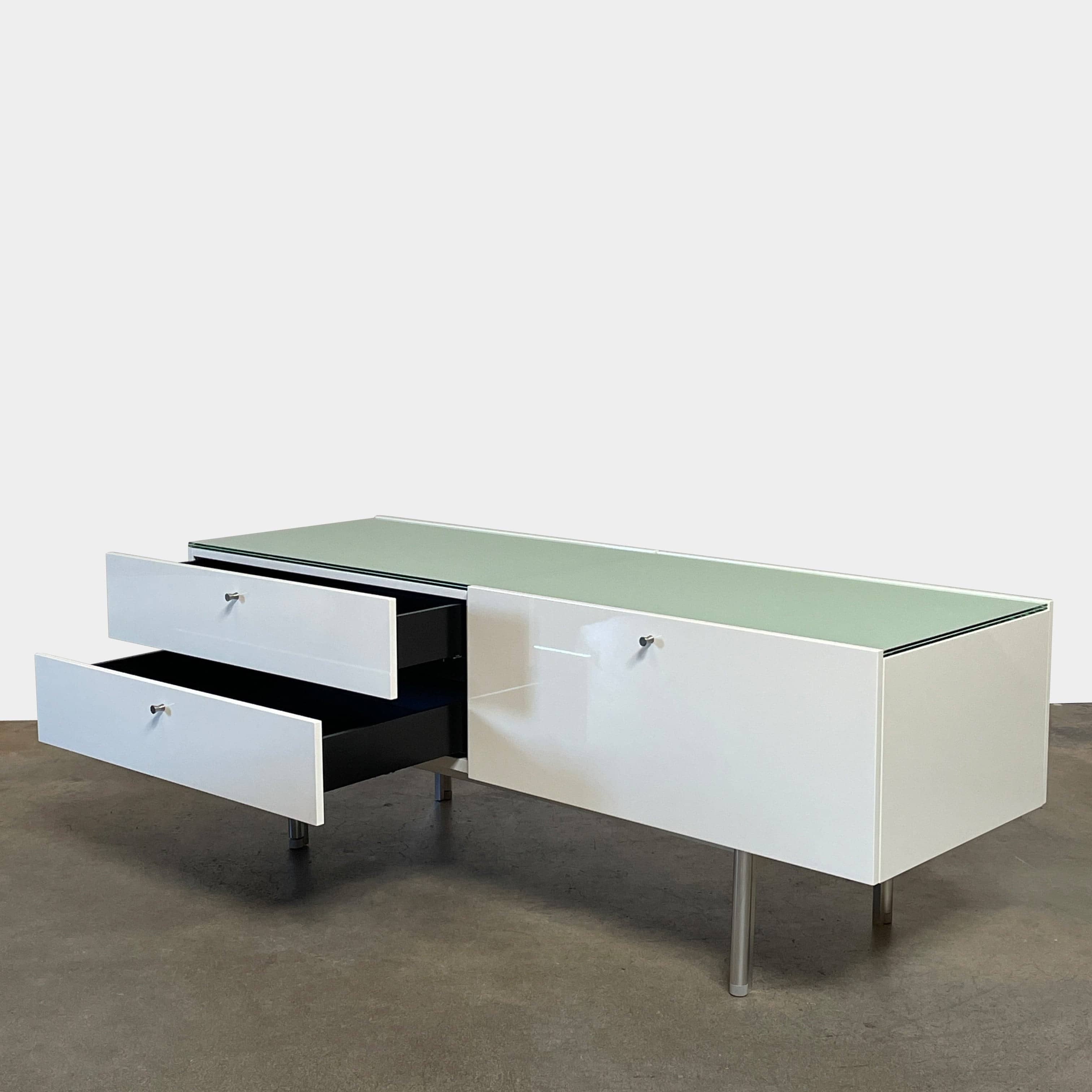The Cassina 255-256 Flat Sideboard in glossy white lacquer features two left drawers, a spacious right compartment, and four metal legs, all by Cassina, shown against a plain background.