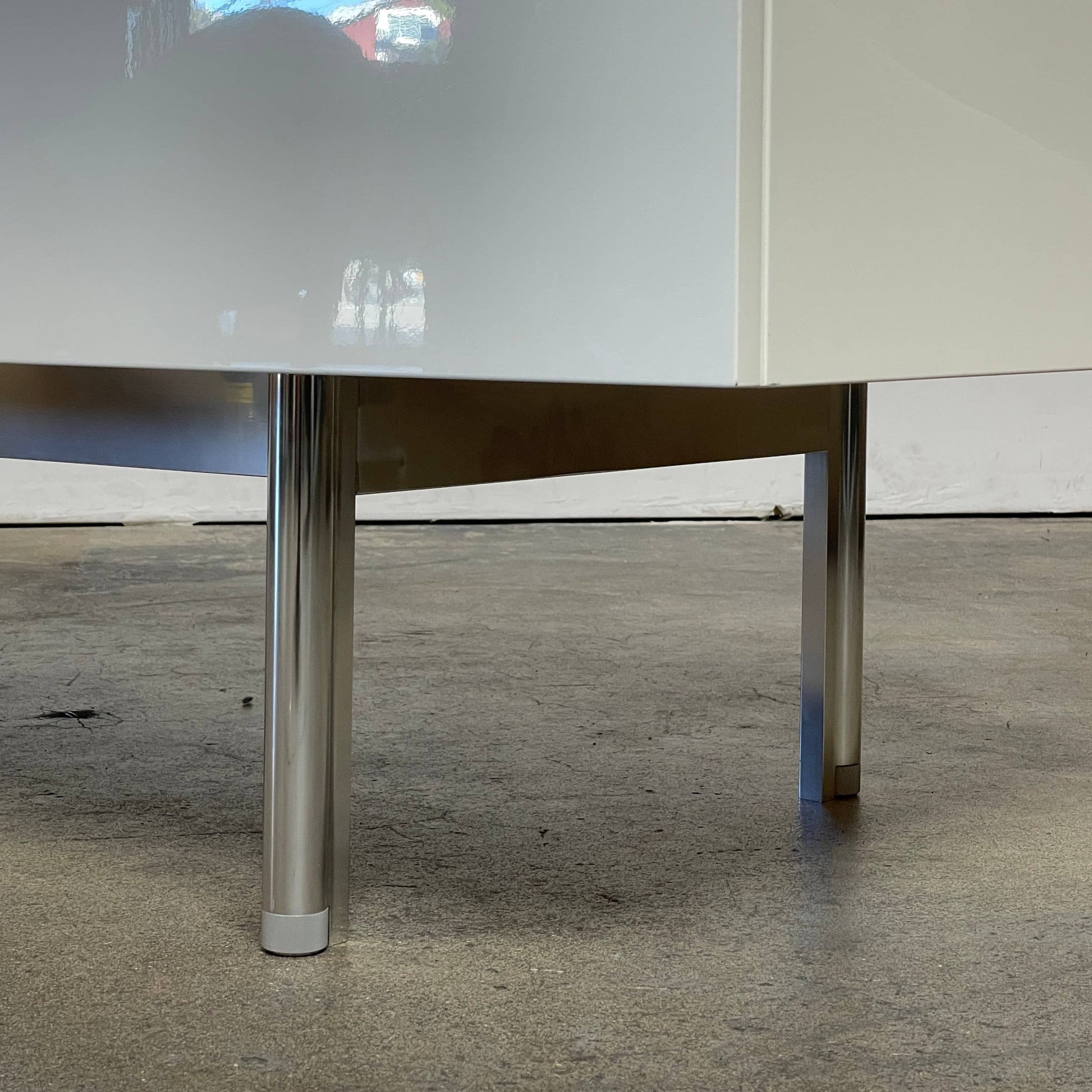 The Cassina 255-256 Flat Sideboard in glossy white lacquer features two left drawers, a spacious right compartment, and four metal legs, all by Cassina, shown against a plain background.
