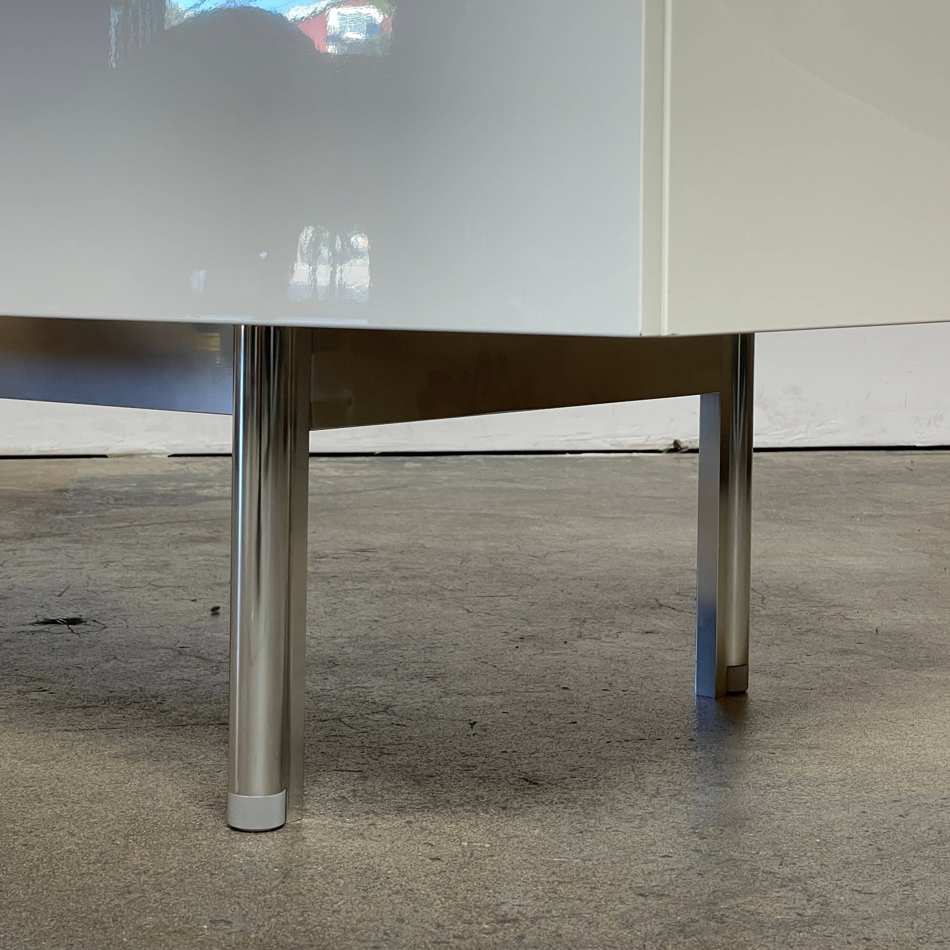 The Cassina 255-256 Flat Sideboard in glossy white lacquer features two left drawers, a spacious right compartment, and four metal legs, all by Cassina, shown against a plain background.
