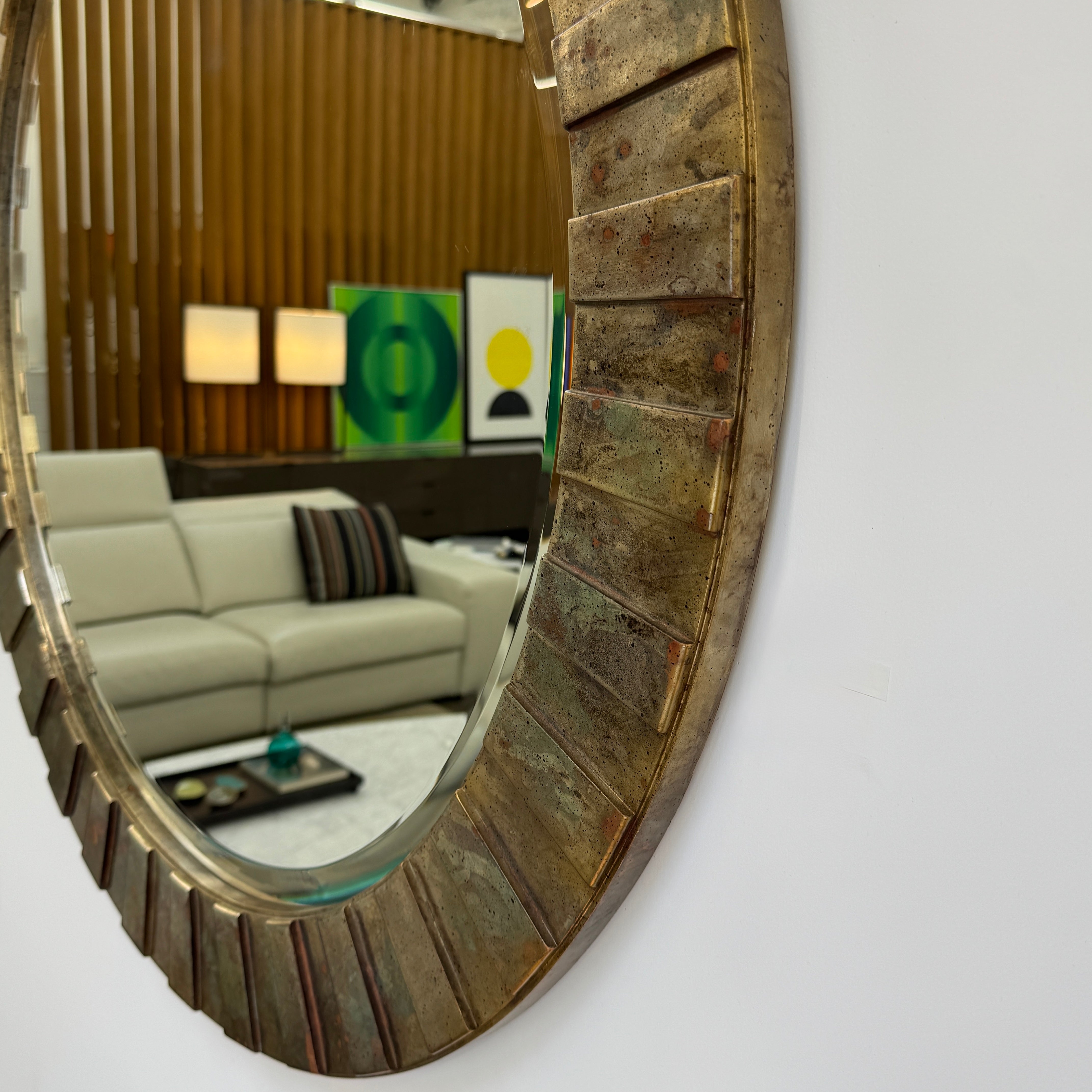 The Vintage Brutalist Mirror 1980s by Vintage features a textured bronze frame, reflecting a modern living room with sofas, wall art, lamps, and a coffee table—an elegant nod to iconic Brutalist design.