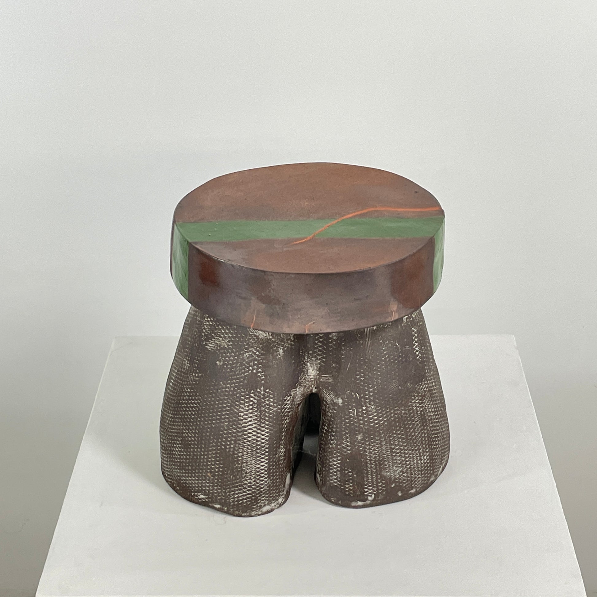 The Allyn Davis Mrs Beastie Ceramic Side Table by Artist features a round, textured design with a wooden top and green stripe. Its woven four-legged base subtly incorporates Kintsugo elements, adding depth and character to the piece.