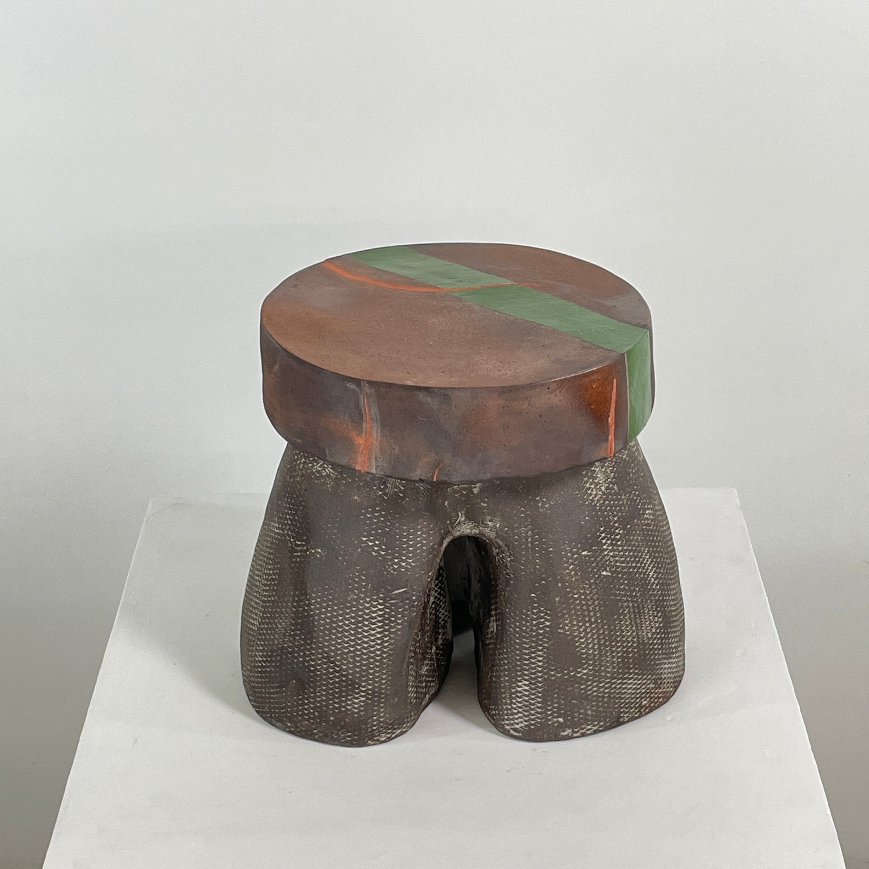 The Allyn Davis Mrs Beastie Ceramic Side Table by Artist features a round, textured design with a wooden top and green stripe. Its woven four-legged base subtly incorporates Kintsugo elements, adding depth and character to the piece.