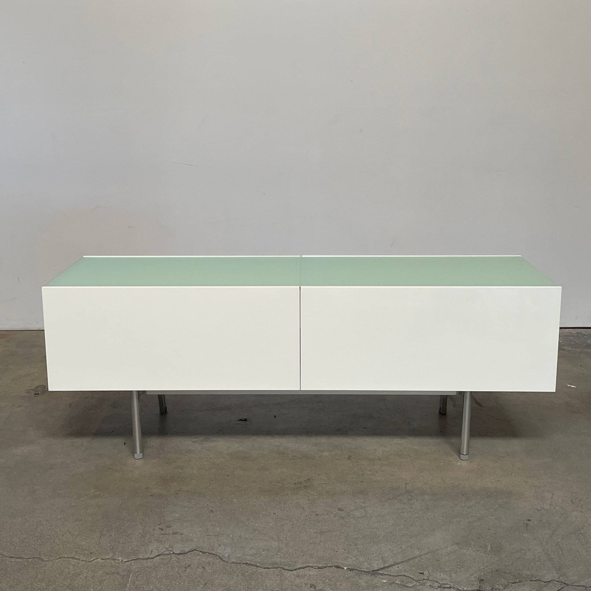 The Cassina 255-256 Flat Sideboard in glossy white lacquer features two left drawers, a spacious right compartment, and four metal legs, all by Cassina, shown against a plain background.