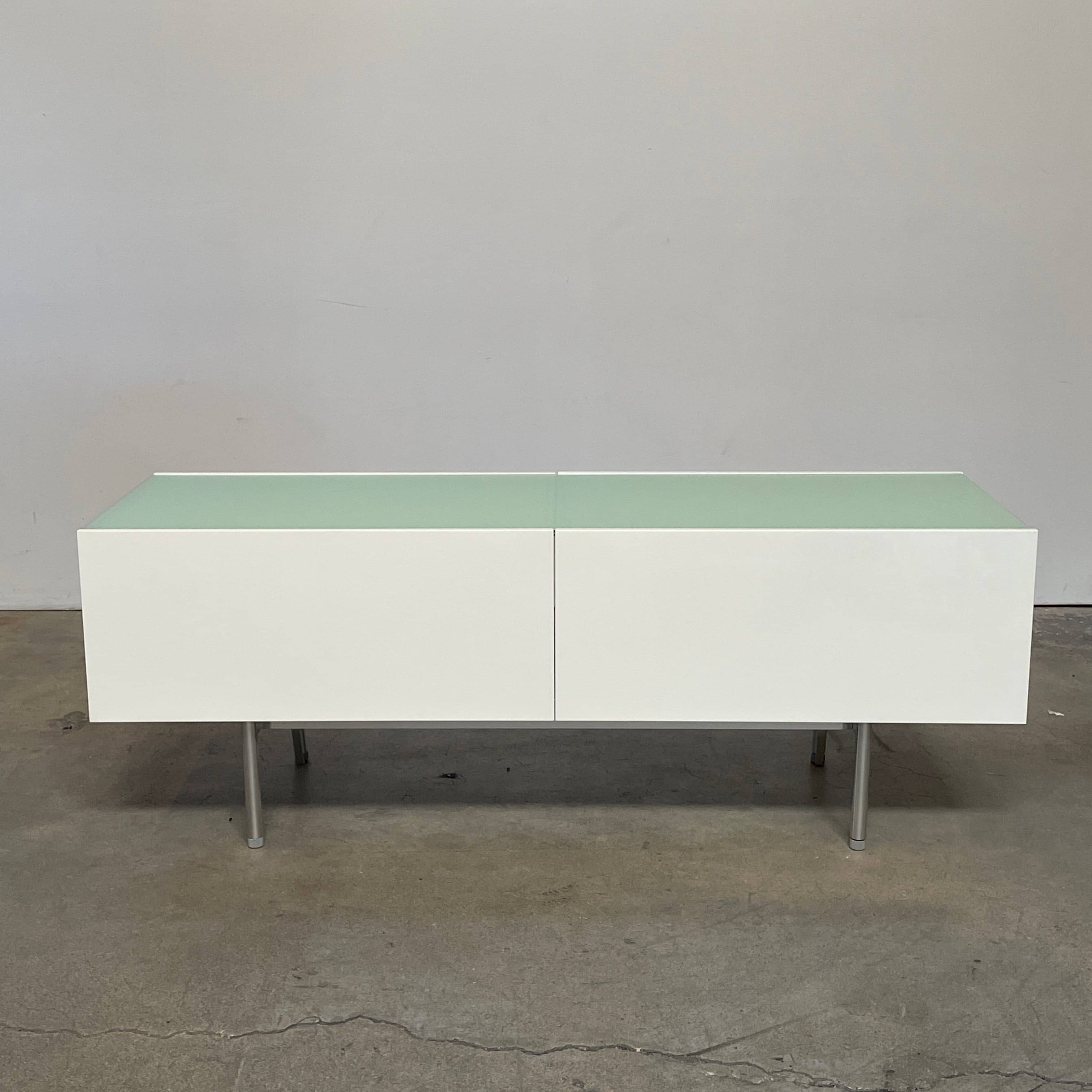 The Cassina 255-256 Flat Sideboard in glossy white lacquer features two left drawers, a spacious right compartment, and four metal legs, all by Cassina, shown against a plain background.