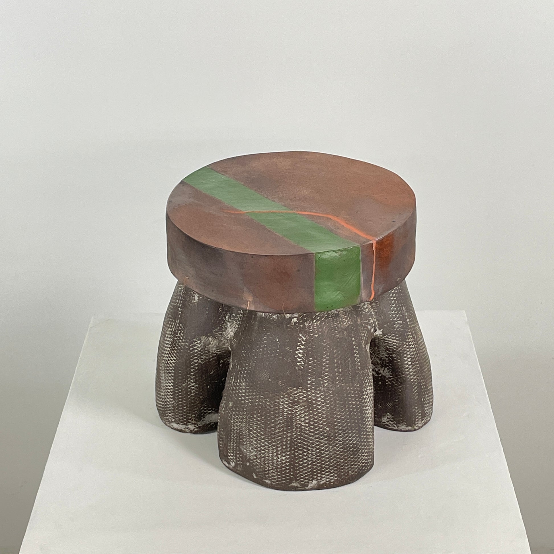 The Allyn Davis Mrs Beastie Ceramic Side Table by Artist features a round, textured design with a wooden top and green stripe. Its woven four-legged base subtly incorporates Kintsugo elements, adding depth and character to the piece.