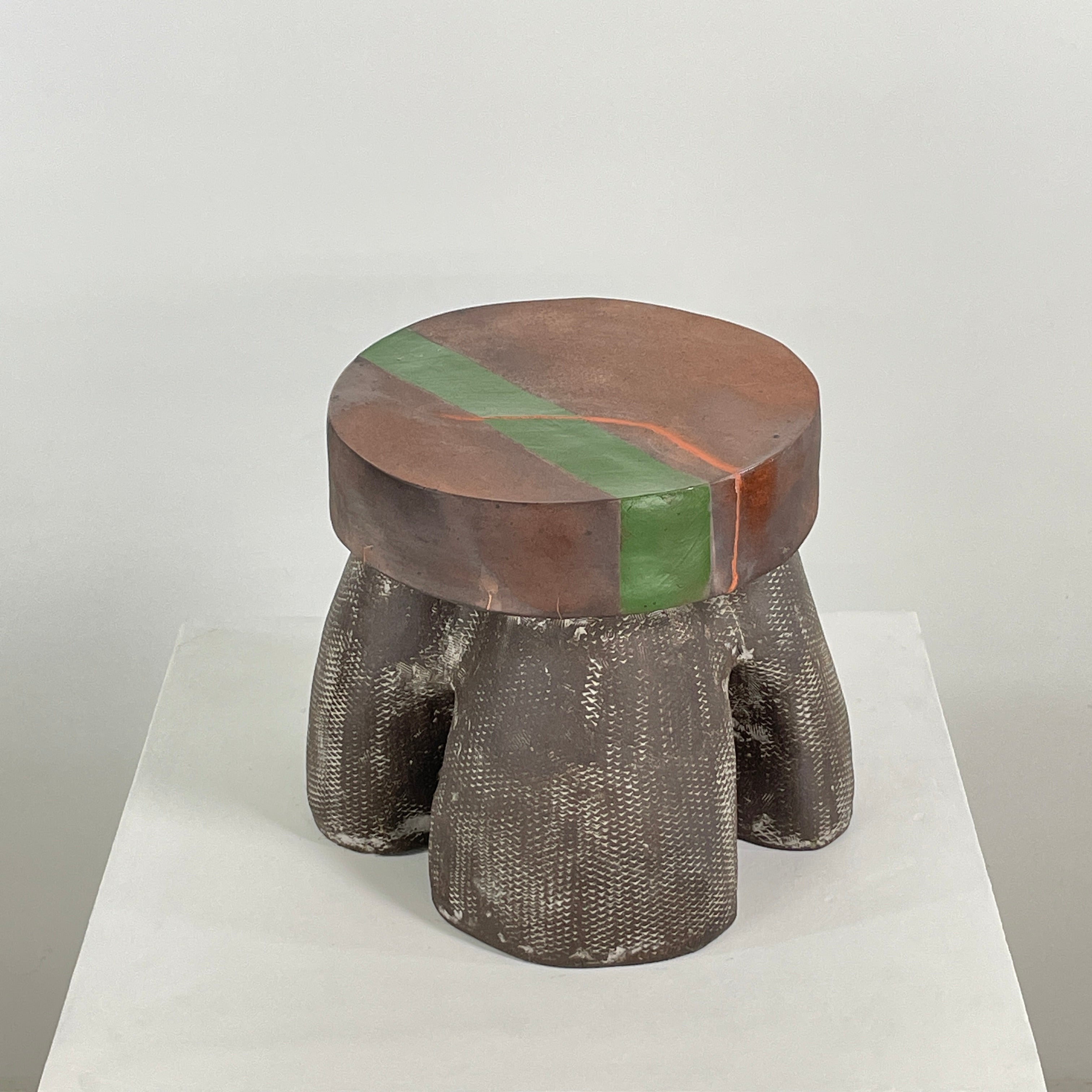 The Allyn Davis Mrs Beastie Ceramic Side Table by Artist features a round, textured design with a wooden top and green stripe. Its woven four-legged base subtly incorporates Kintsugo elements, adding depth and character to the piece.