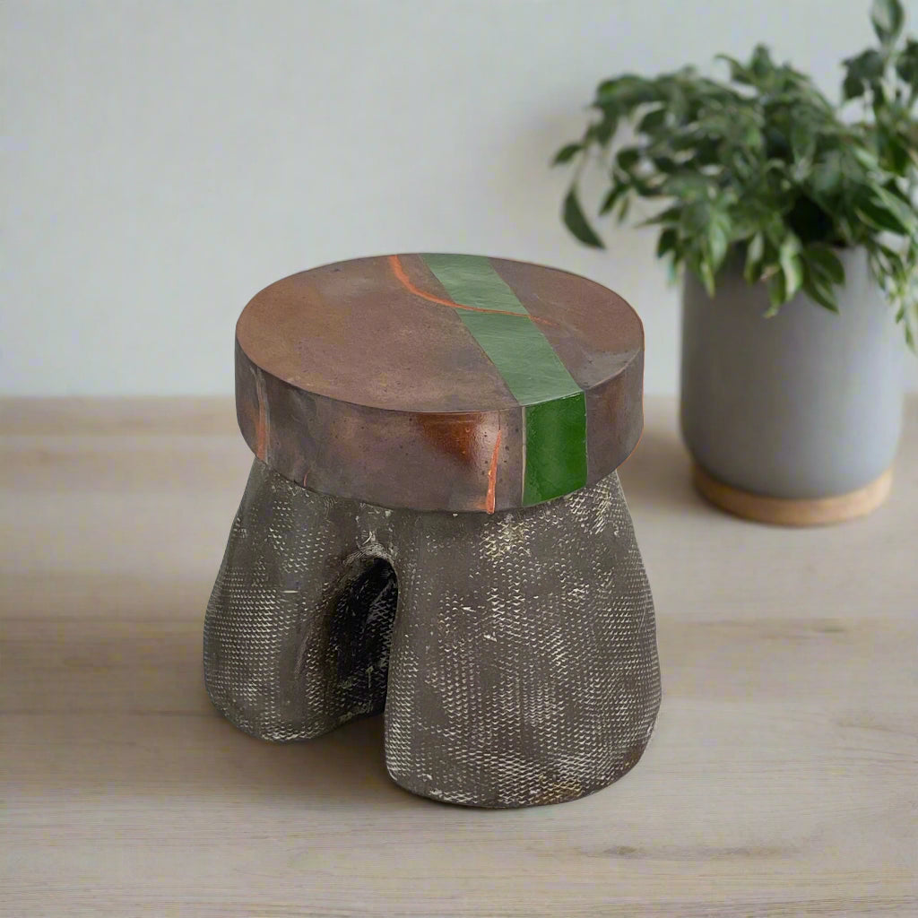 The Allyn Davis Mrs Beastie Ceramic Side Table by Artist features a round, textured design with a wooden top and green stripe. Its woven four-legged base subtly incorporates Kintsugo elements, adding depth and character to the piece.