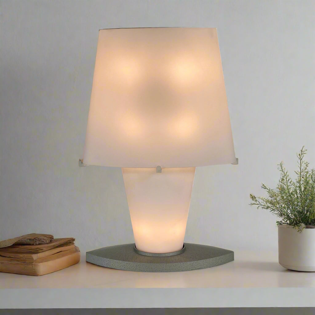 The Fontana Arte 3064 Table Light by Fontana Arte, echoing Daniela Puppa's designs, boasts a wide conical shade for a warm glow. It sits elegantly on a white surface against a plain backdrop, capturing the essence of postmodern art.