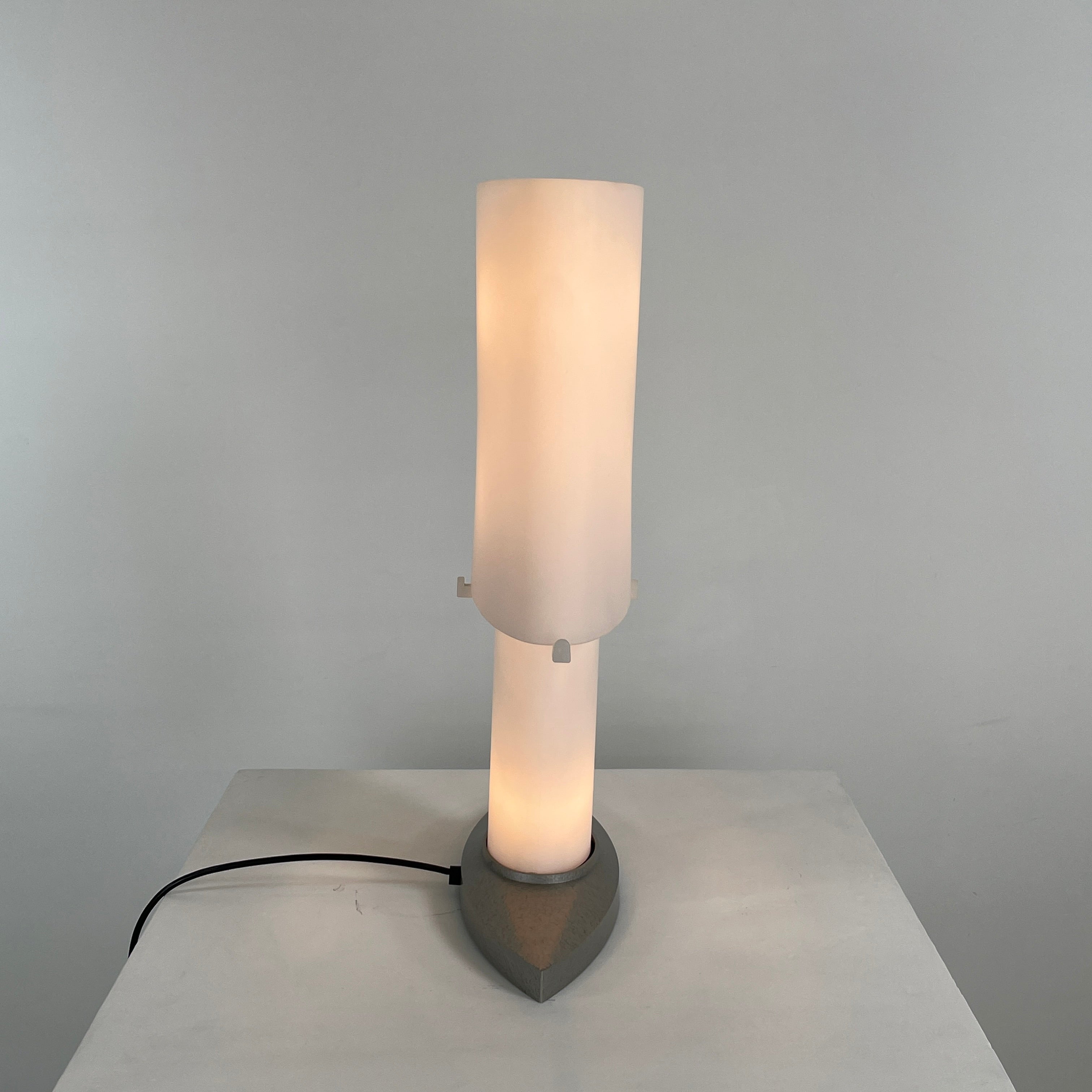 The Fontana Arte 3064 Table Light by Fontana Arte, echoing Daniela Puppa's designs, boasts a wide conical shade for a warm glow. It sits elegantly on a white surface against a plain backdrop, capturing the essence of postmodern art.